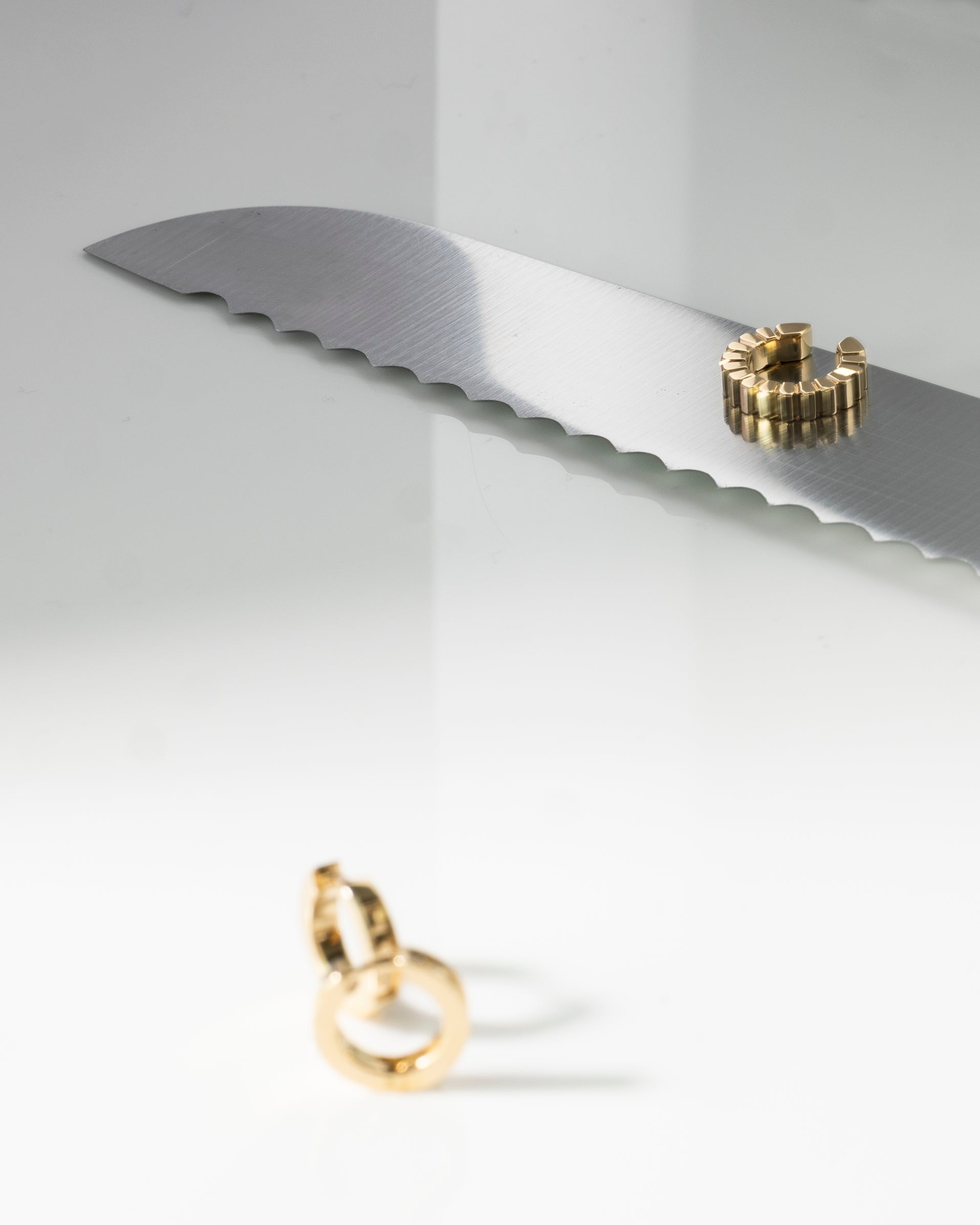 Gold ridged ear cuff on a white surface with a knife blade