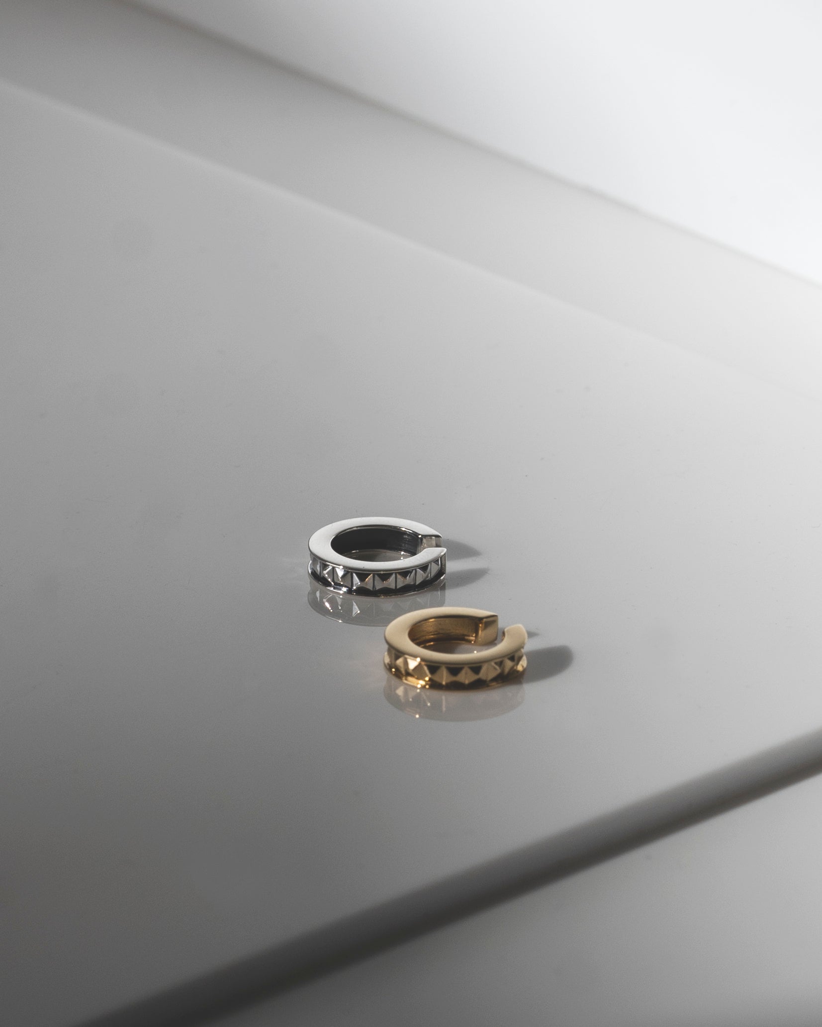 ear cuffs gold and silver with studs flatlay white reflective surface