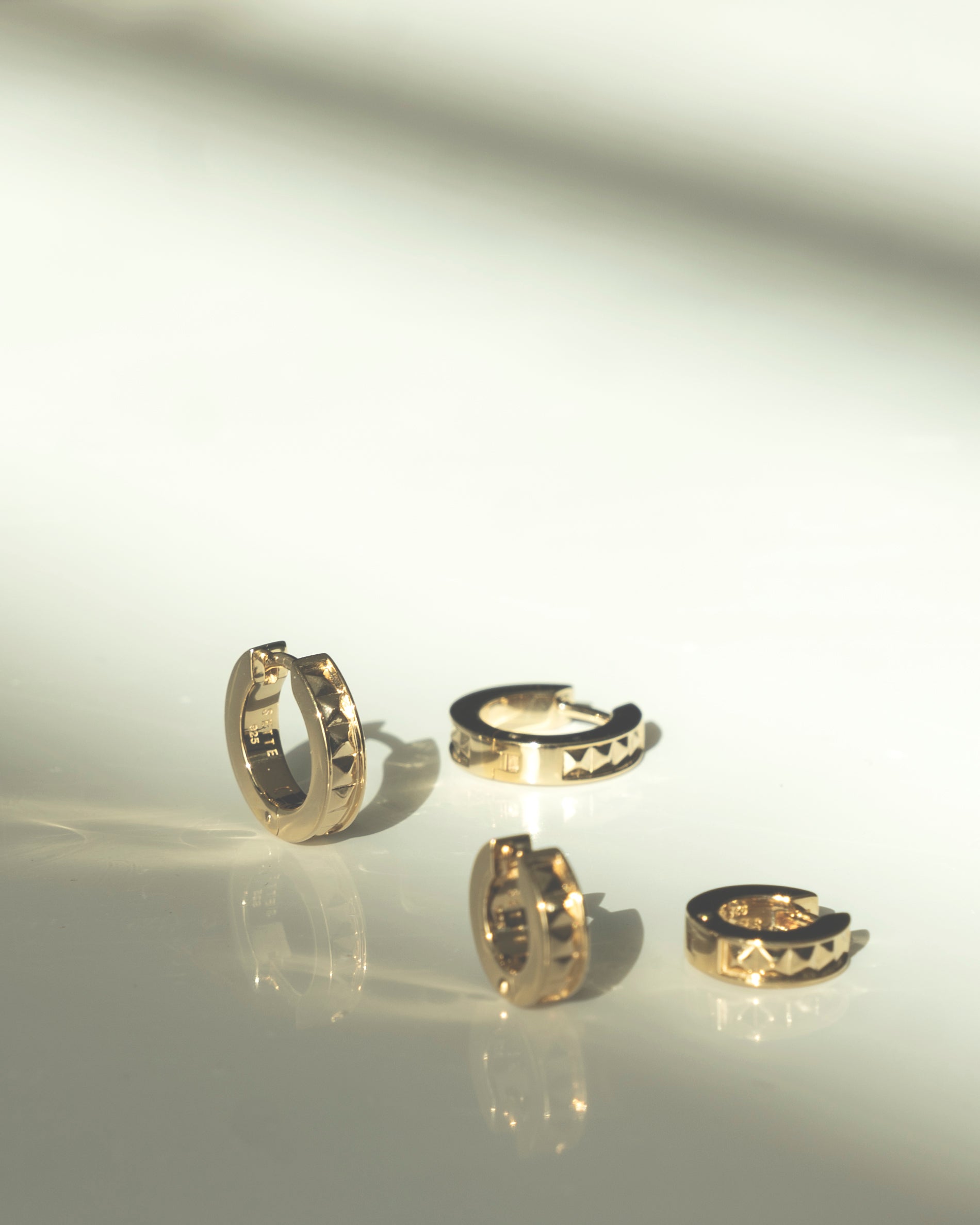air of gold hoops huggies with studs on soft light background with shadow
