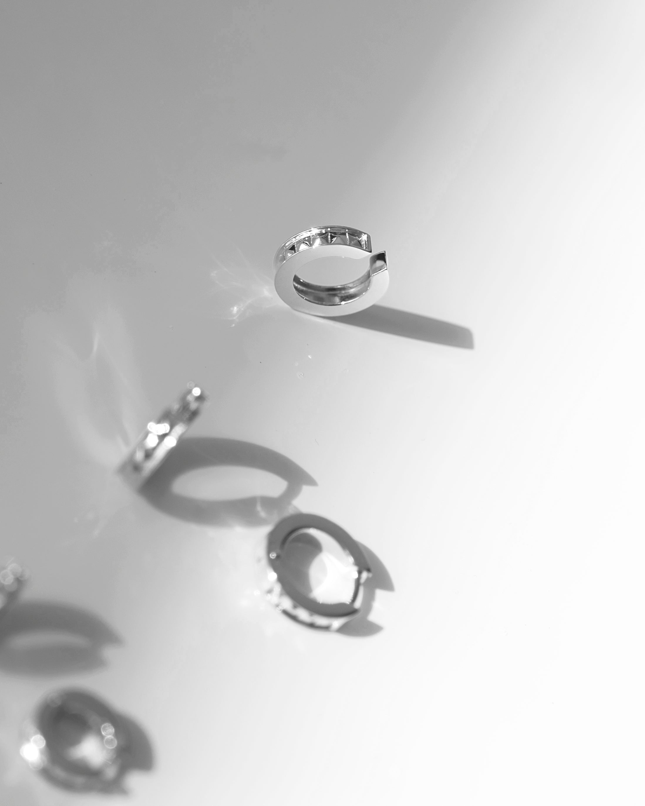 Silver ear cuff with studs and rhodium plating on white surface with shadow