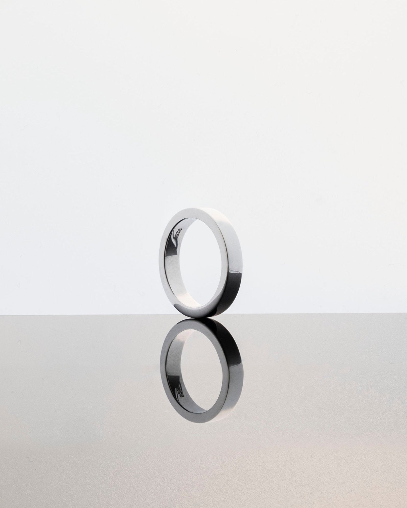 polished silver band ring with reflection on mirrored grey surface