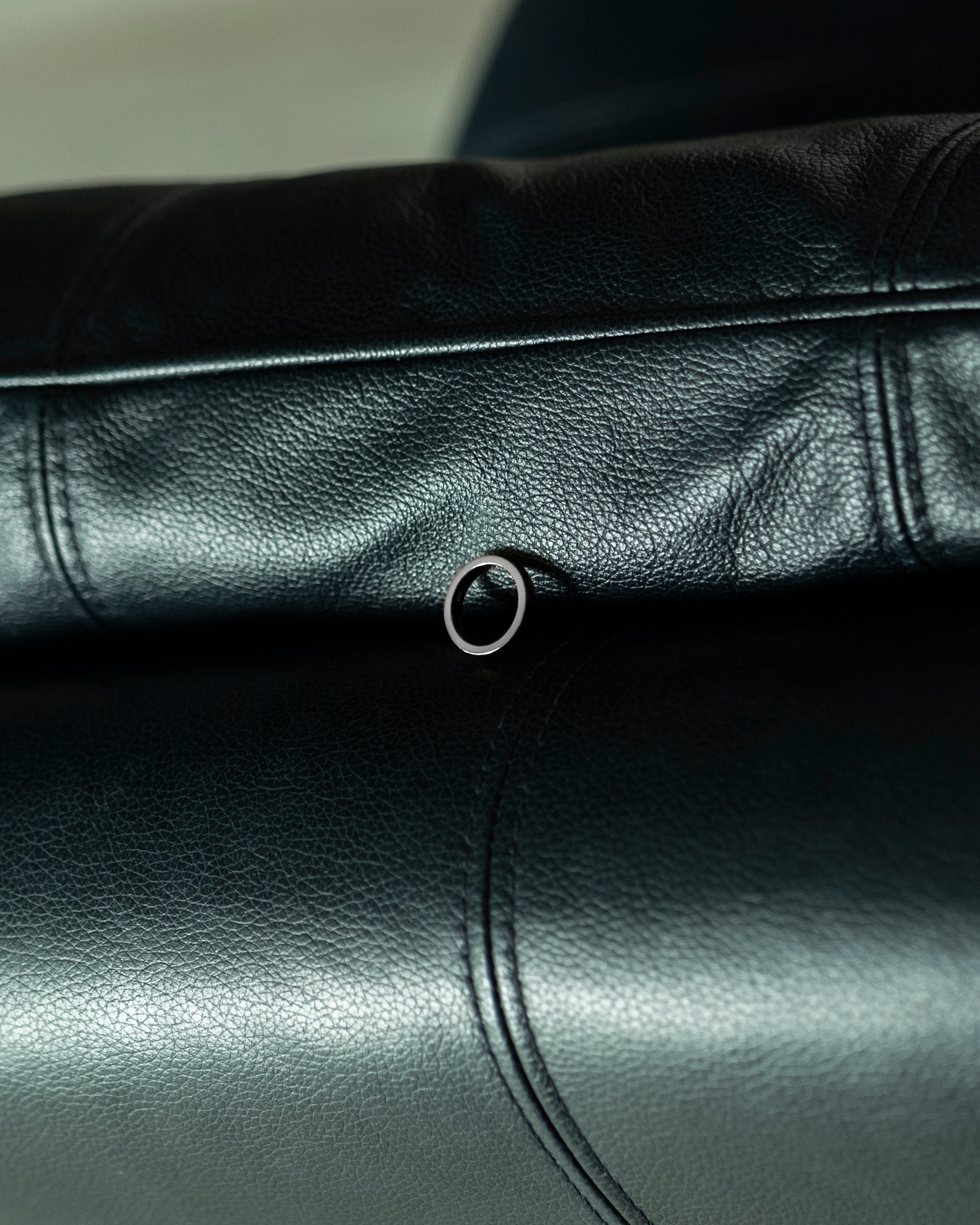 polished silver band ring laid on navy leather sofa with stitching