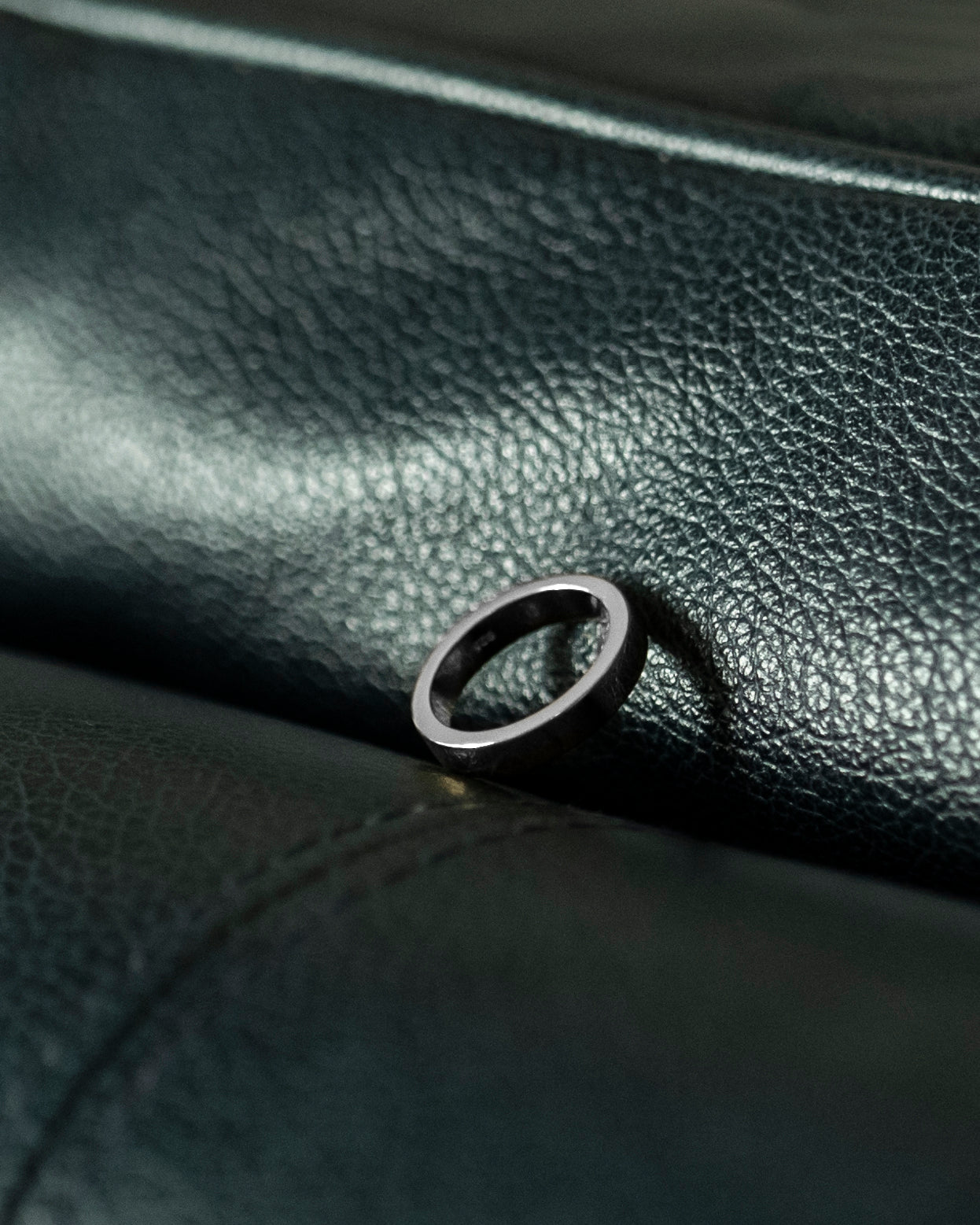 polished silver band ring closeup on navy leather with stitching