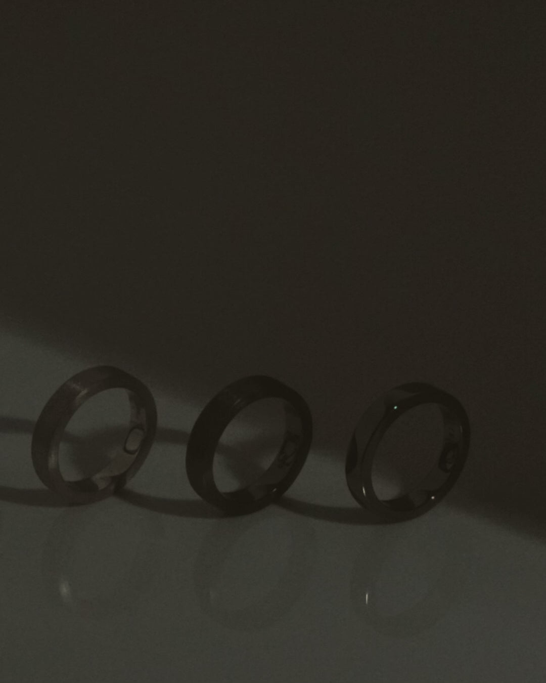 three black and silver band rings on white reflective surface
