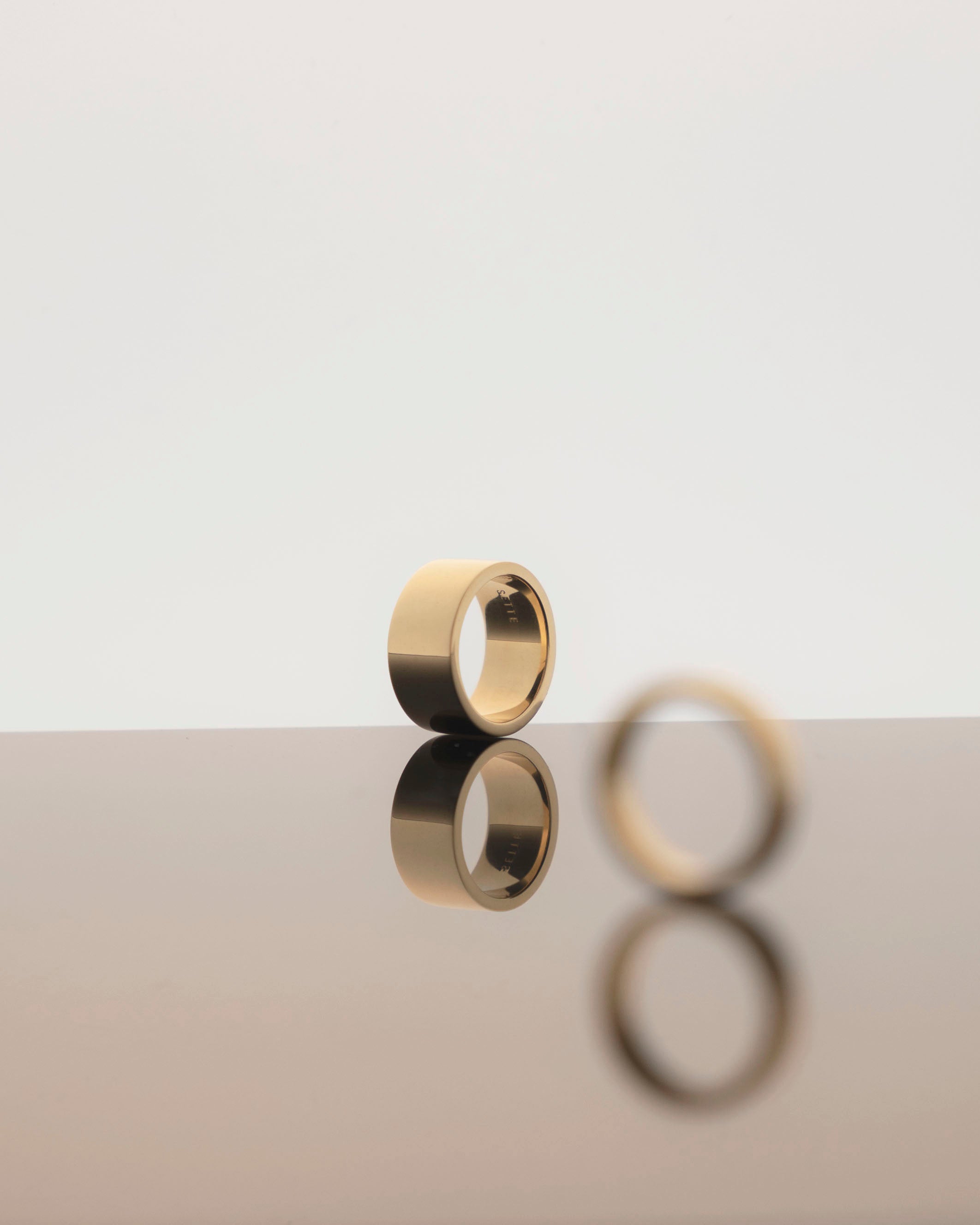 chunky gold ring on light grey reflective background