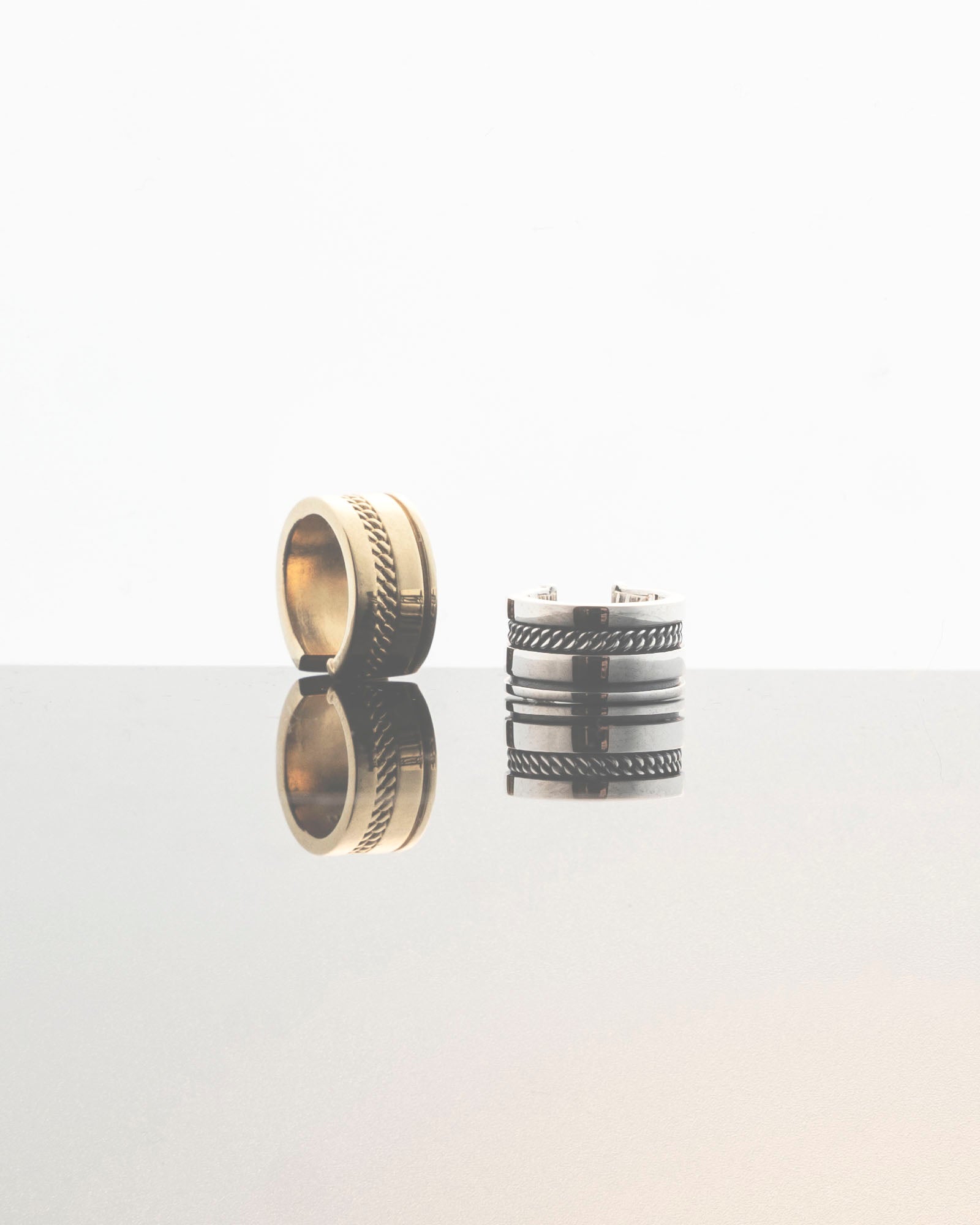 unisex gold and silver ear cuffs with chain detail reflecting on grey mirror surface