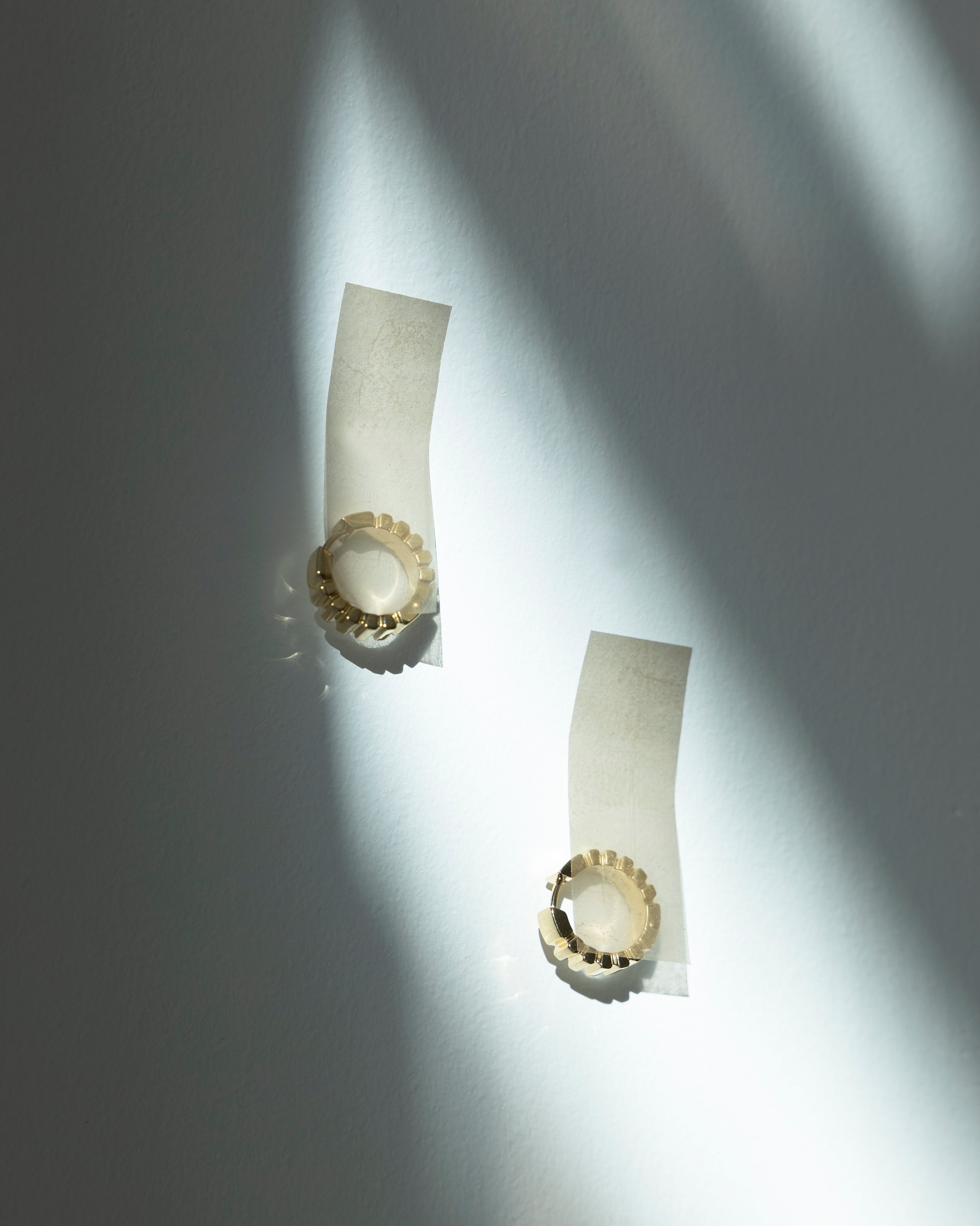 studio sette gold earrings on white tape against a grey background with dappled sunlight