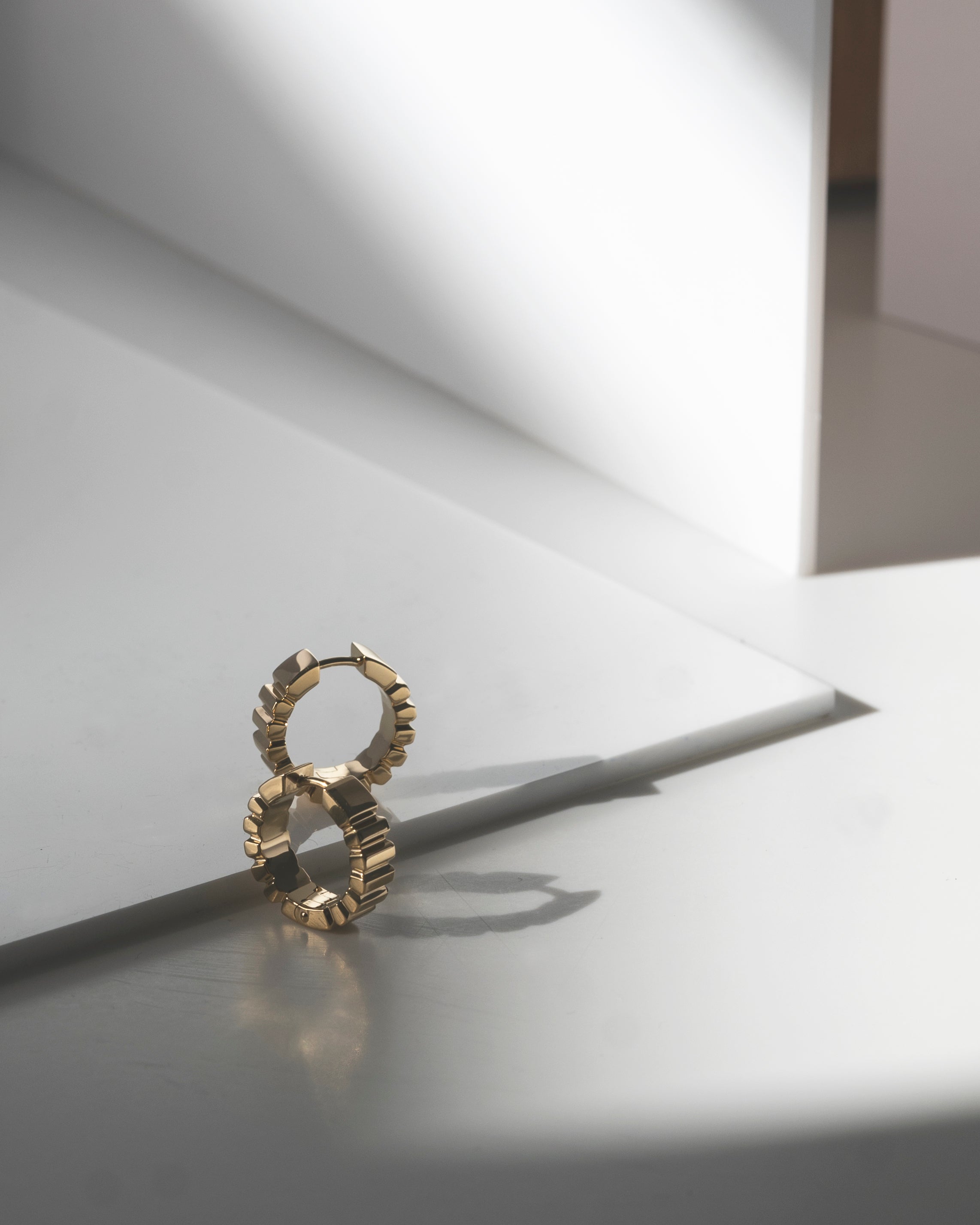 studio sette gold hoops earrings 18kt gold on a reflective surface with soft lighting