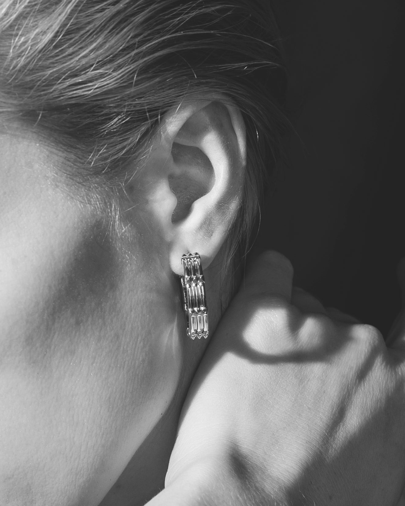studio sette large hoop earrings closeup on model ear with hand on neck monochrome