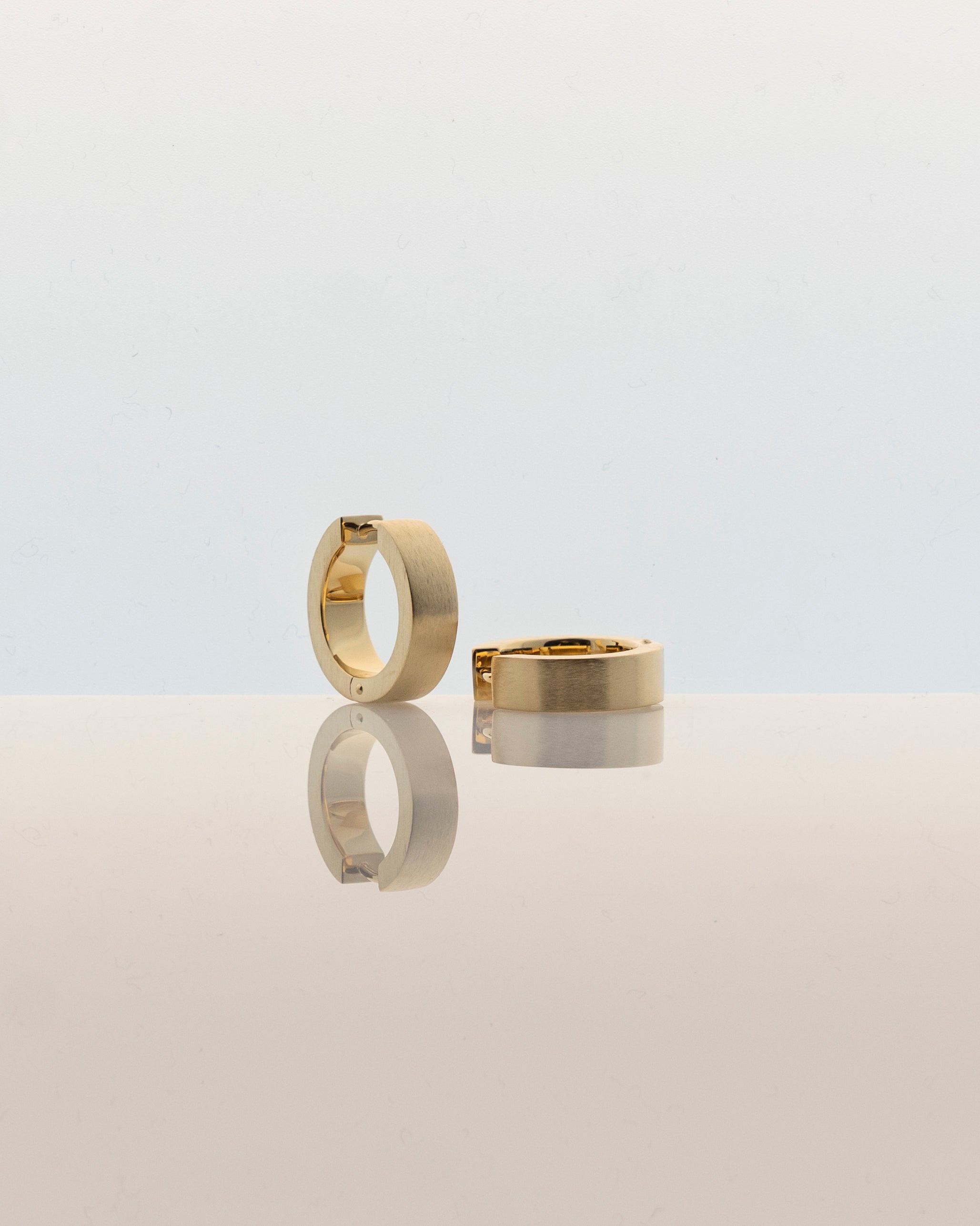 pair gold hoops brushed reflecting on creamy white surface