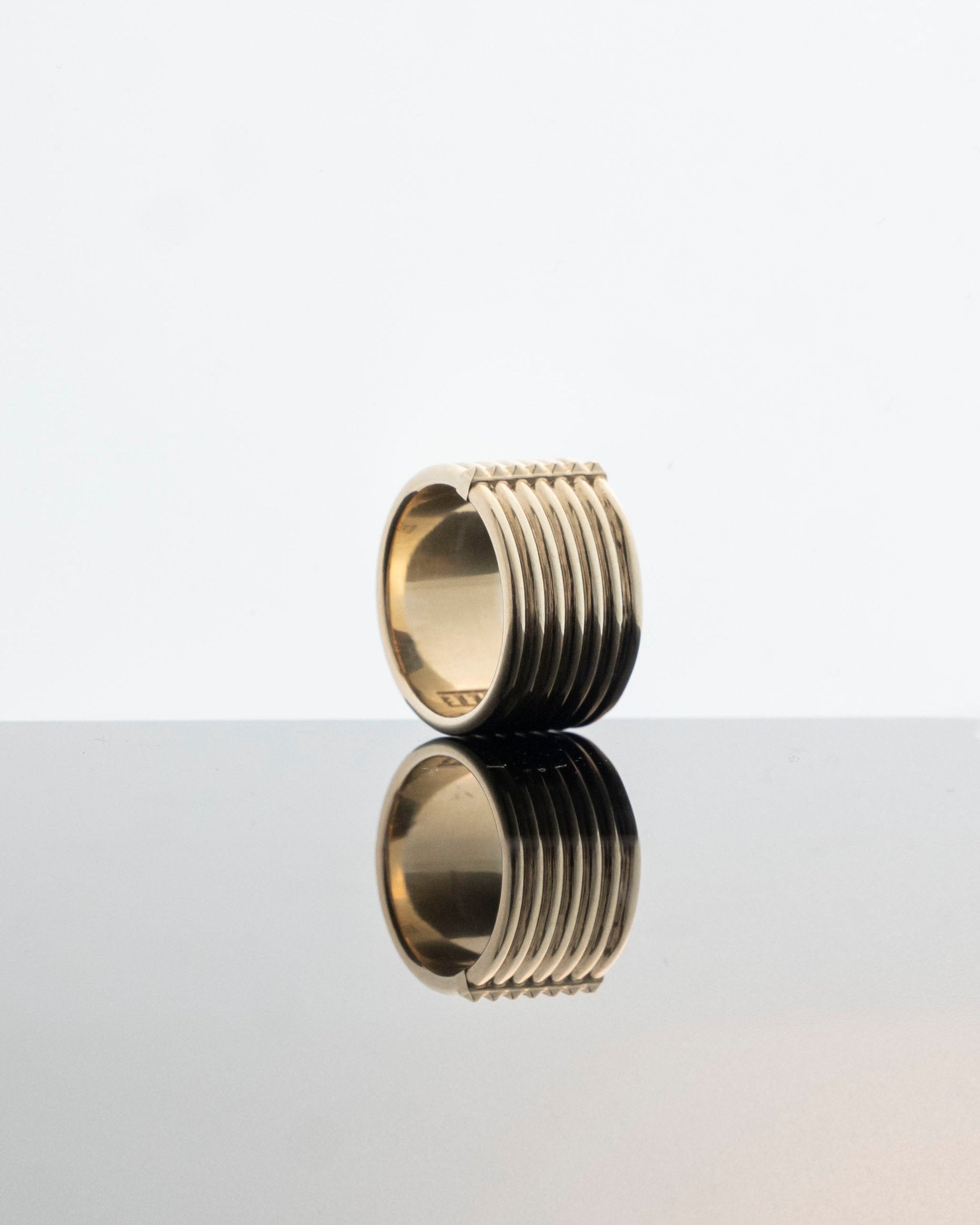 unisex chunky gold ring with pyramid stud detailing reflecting on light grey mirror surface