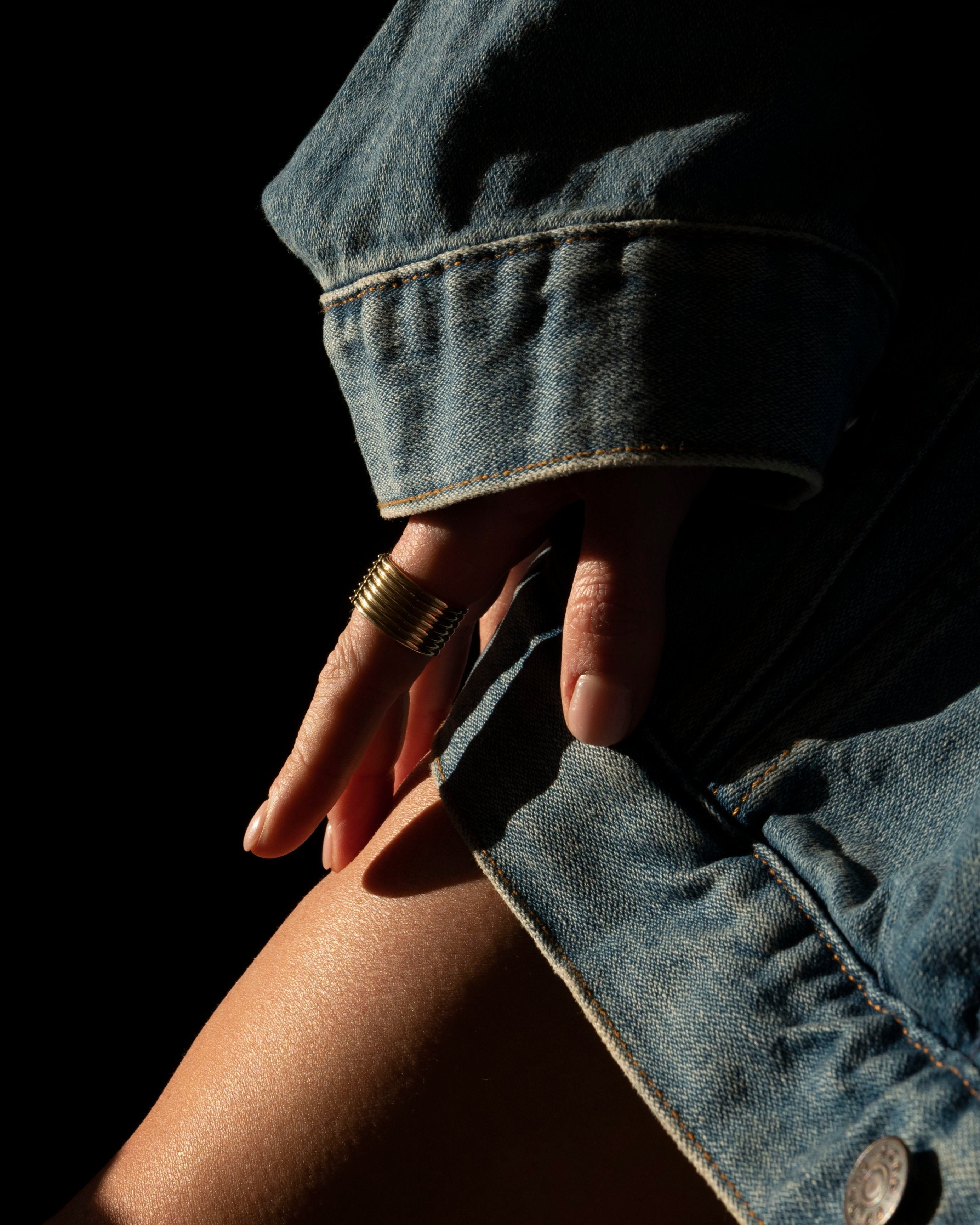 Unisex Gold Ring closeup on model hand touchign bare skin on leg and wearing oversized denim jacket