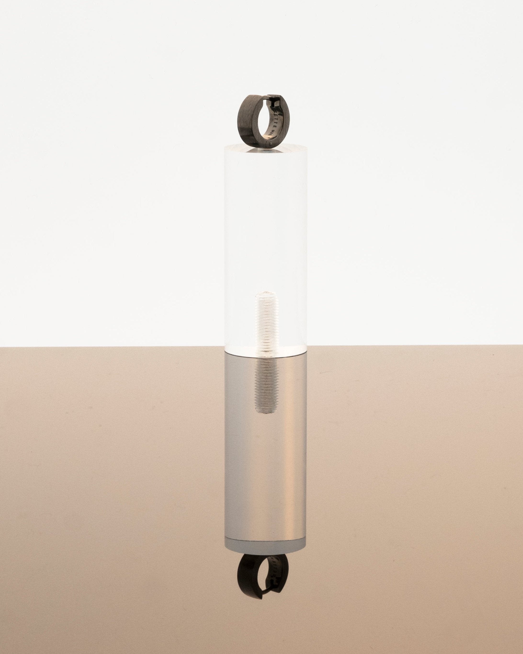 small black hoop earring on perspex podium reflecting on grey mirror surface