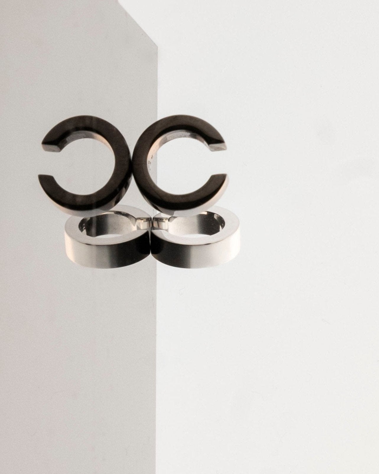 pair of ear cuffs black and silver reflecting on light grey mirror surface