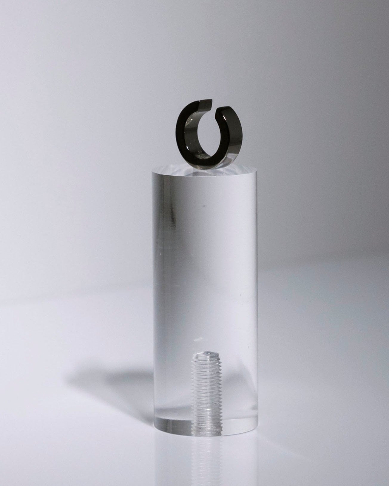 black ruthenium ear cuff on clear podium on light grey background studio flatlay