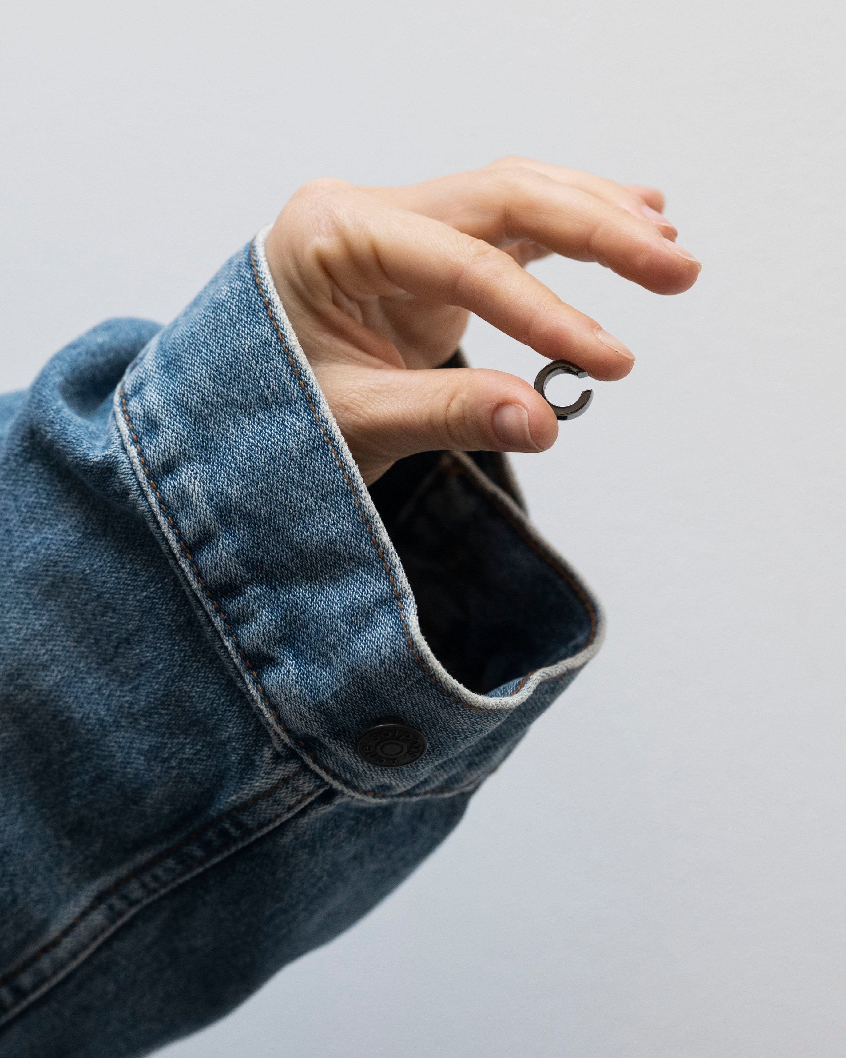 black ear cuff in finger tips and denim sleeve by studio sette