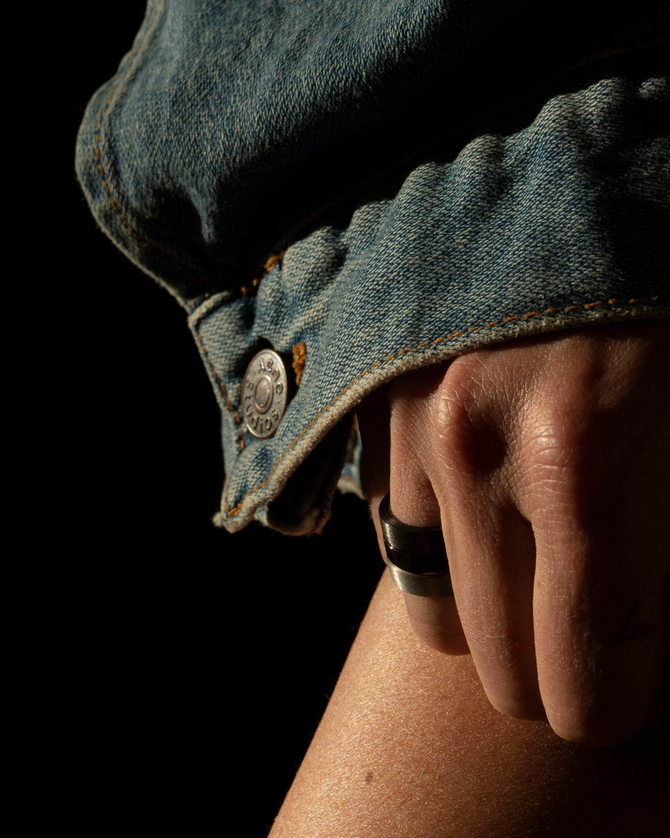 studio sette band rings black and silver stacked on model hand closeup with denim sleeve