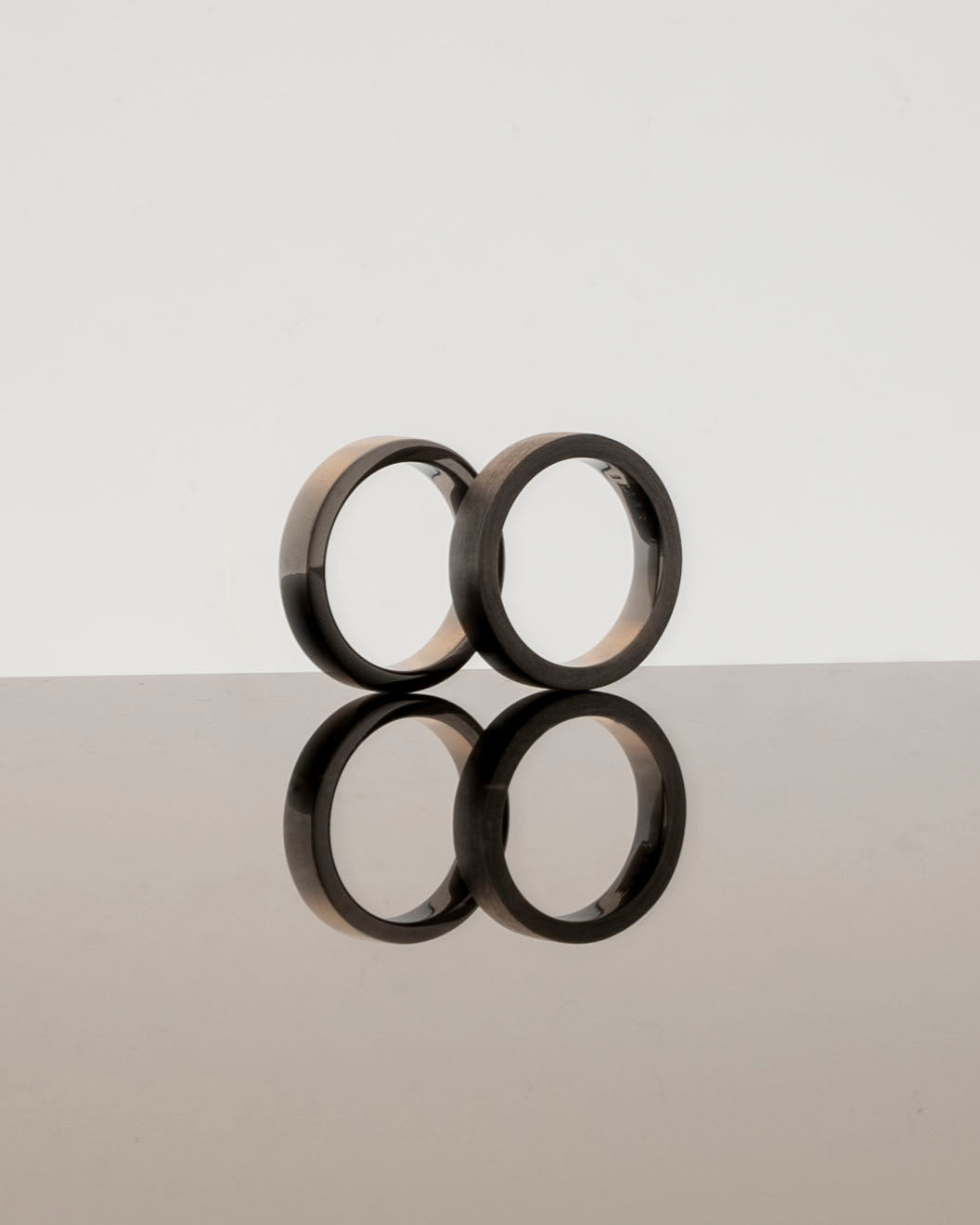 two polished band rings reflecting on a light grey mirrored surface