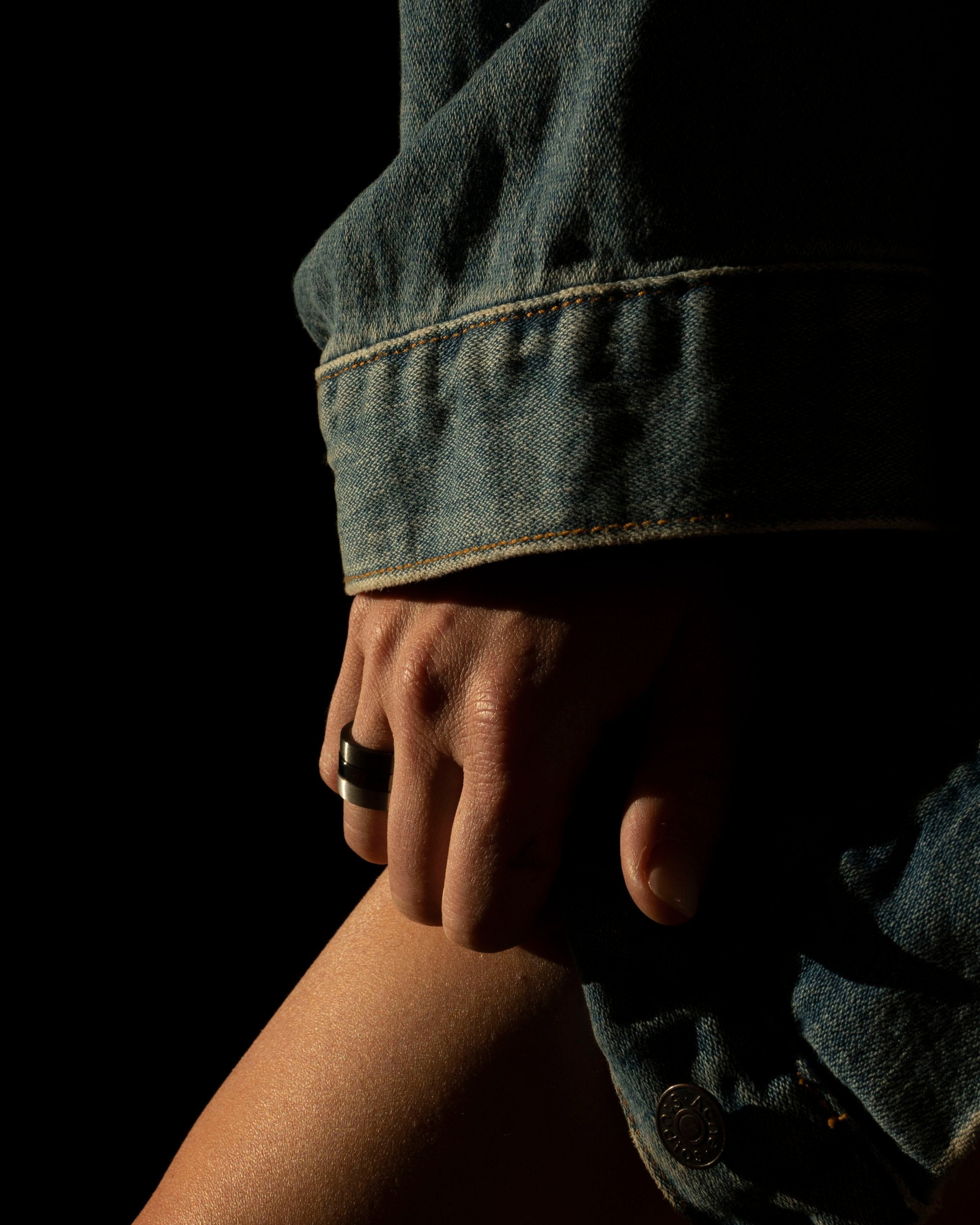black band ring stacked with silver on a model hand resting on leg with denim jacket