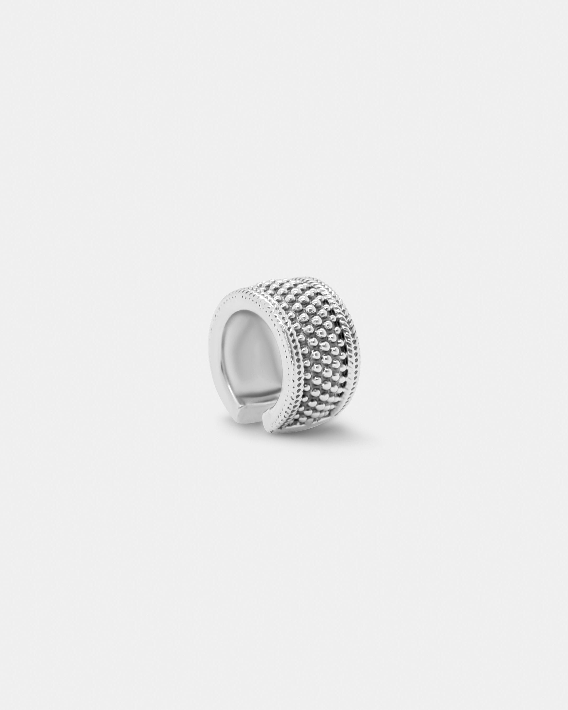 a silver ear cuff with stud detailing and chunky fit on white background by studio sette
