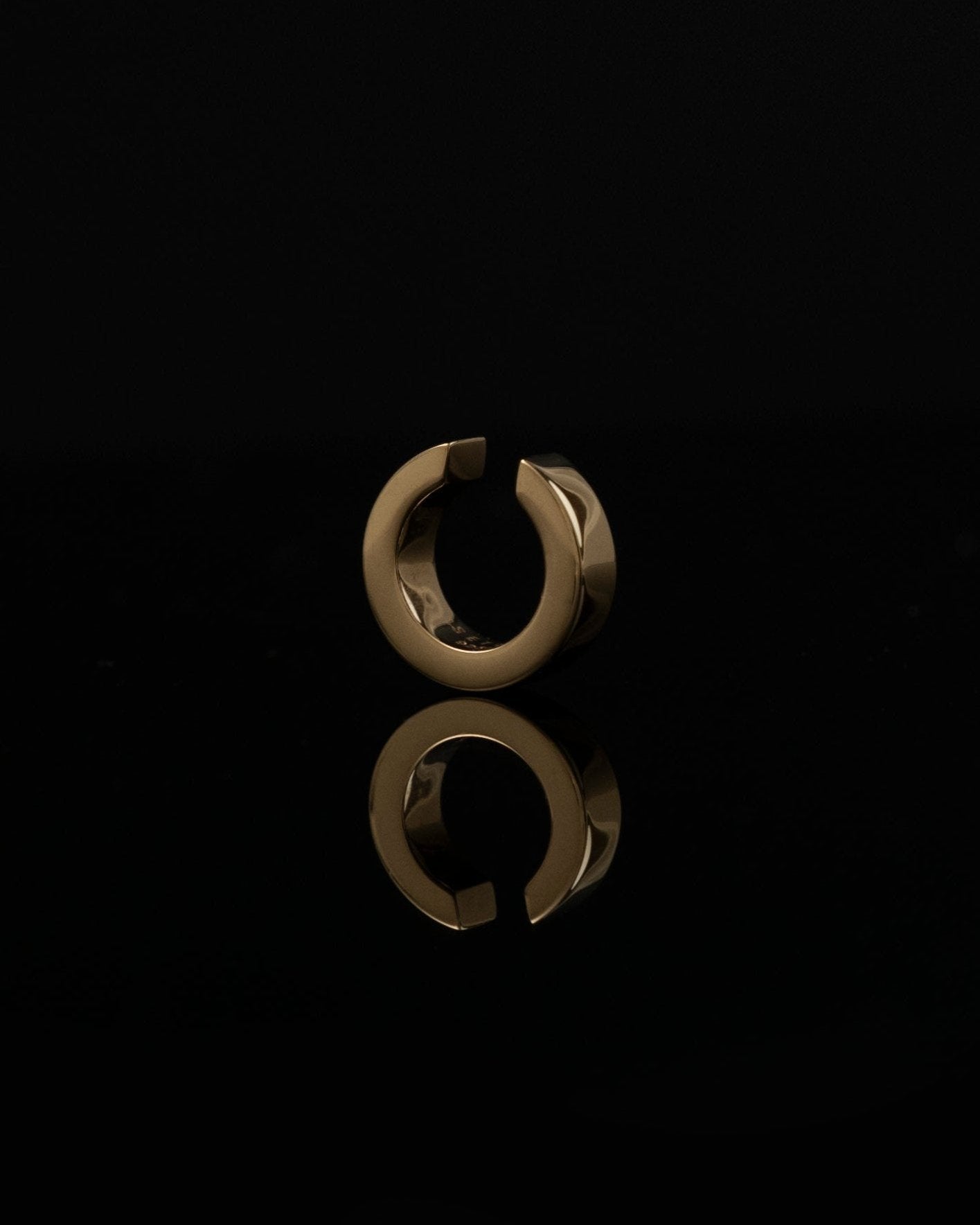 gold ear cuff reflecting on black surface by studio sette