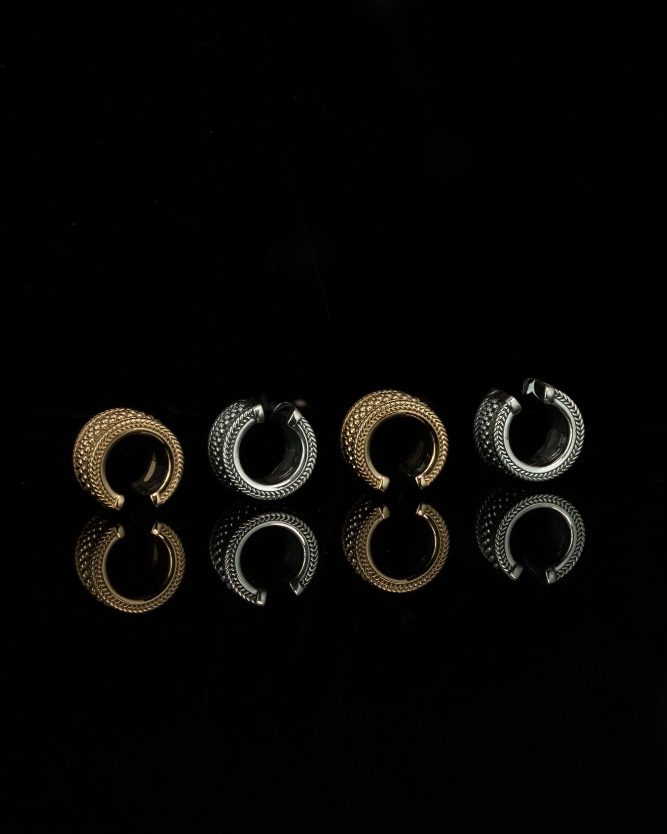 silver and gold ear cuffs in a row on a black reflective background