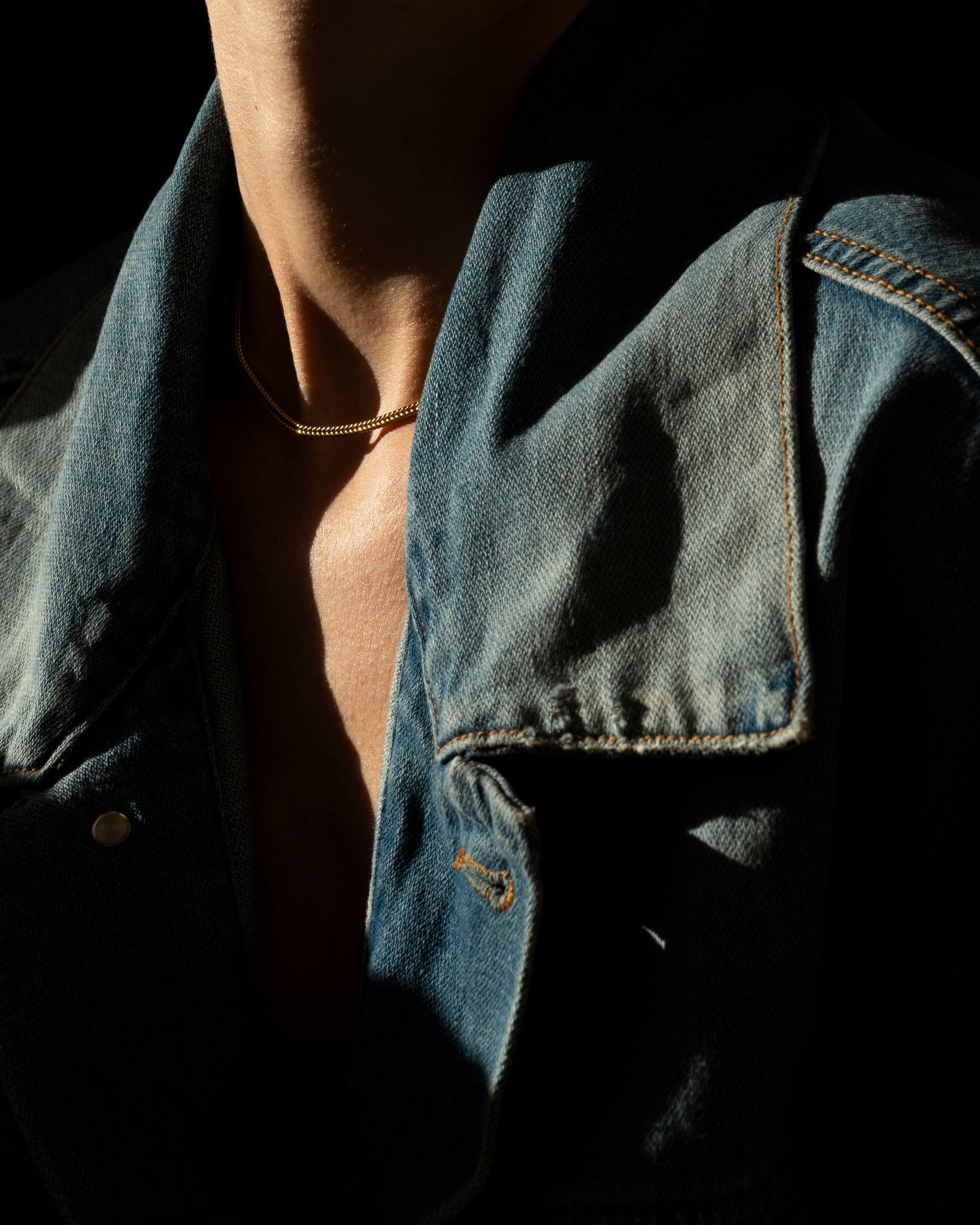 gold fox chain on model's bare skin on neck wearing denim jacket