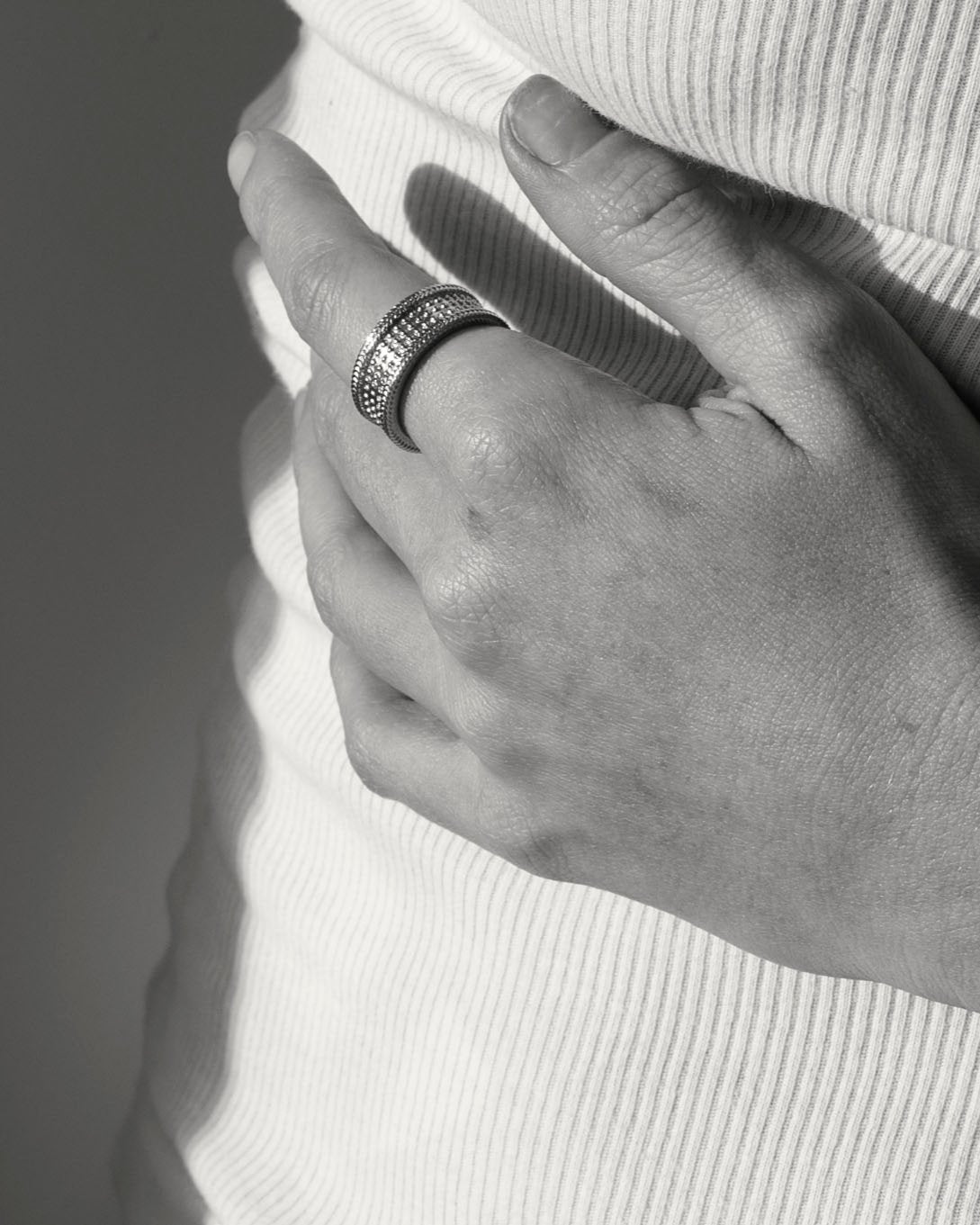 Gold unisex ring closeup on hand resting against white vest top in monochrome