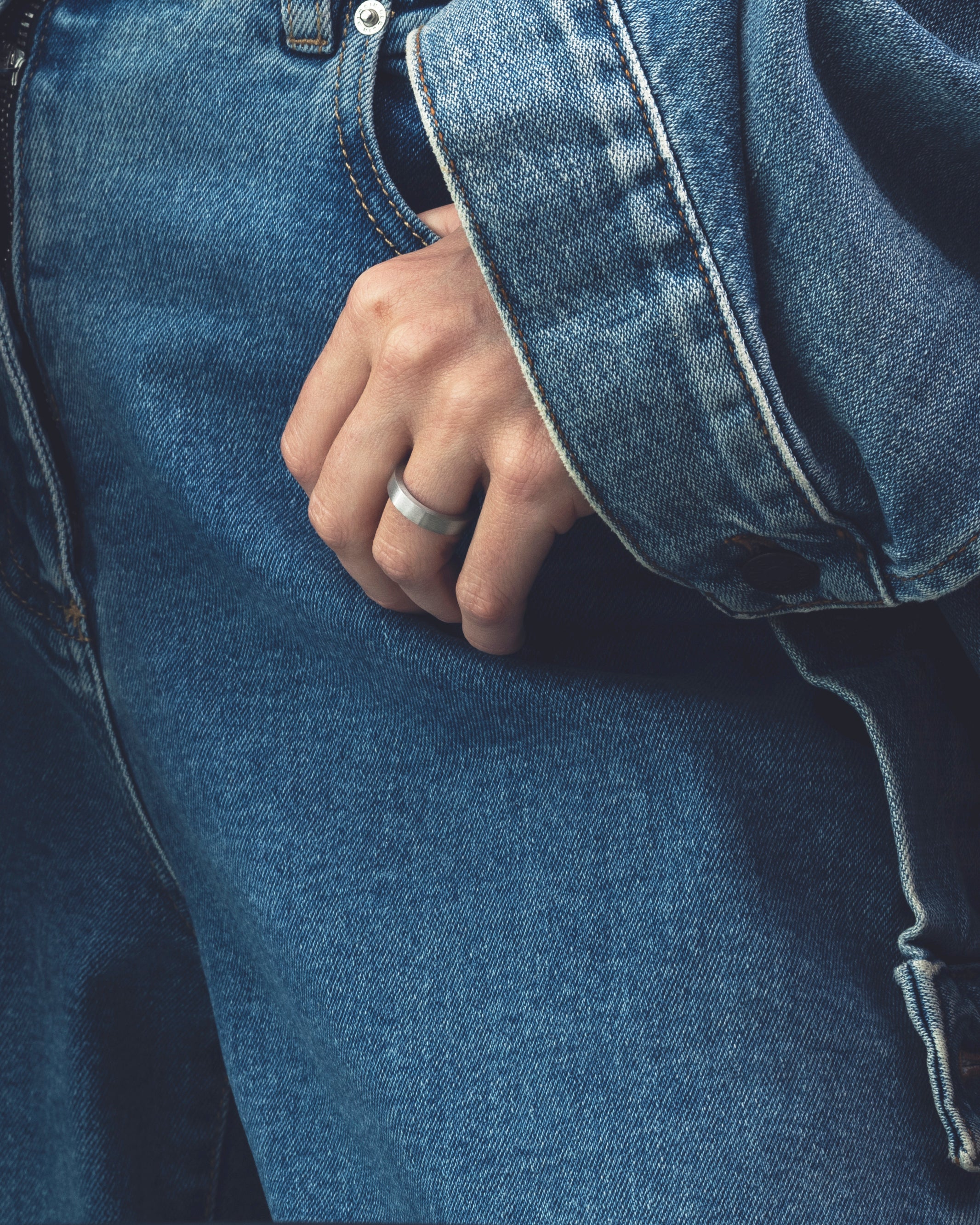 Hand wearing a silver band ring with a blue denim jacket and jeans