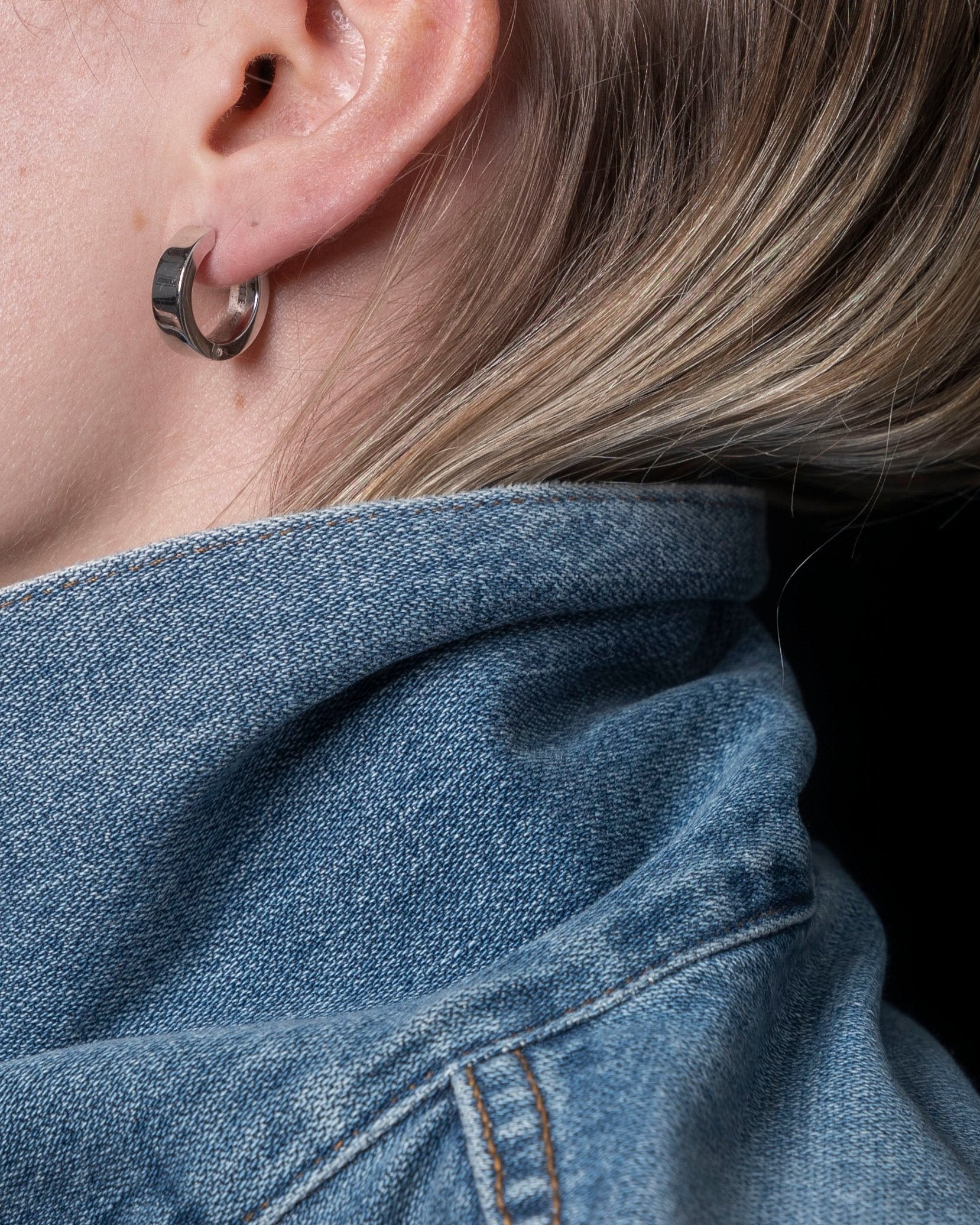 closeup of polished silver earring on model ear wearing denim collar