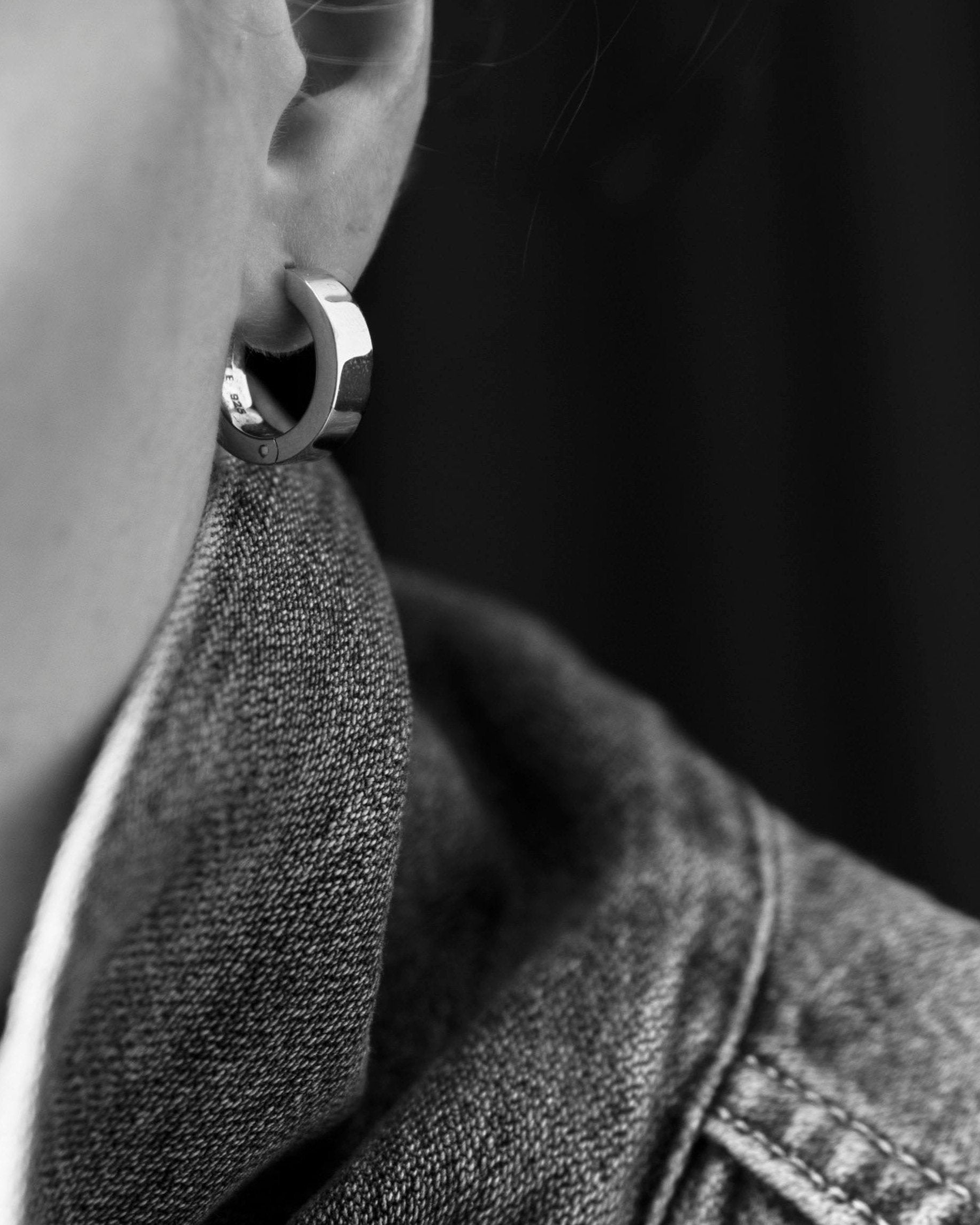 closeup of unisex polished silver earring on model's ear wearing denim collar monochrome
