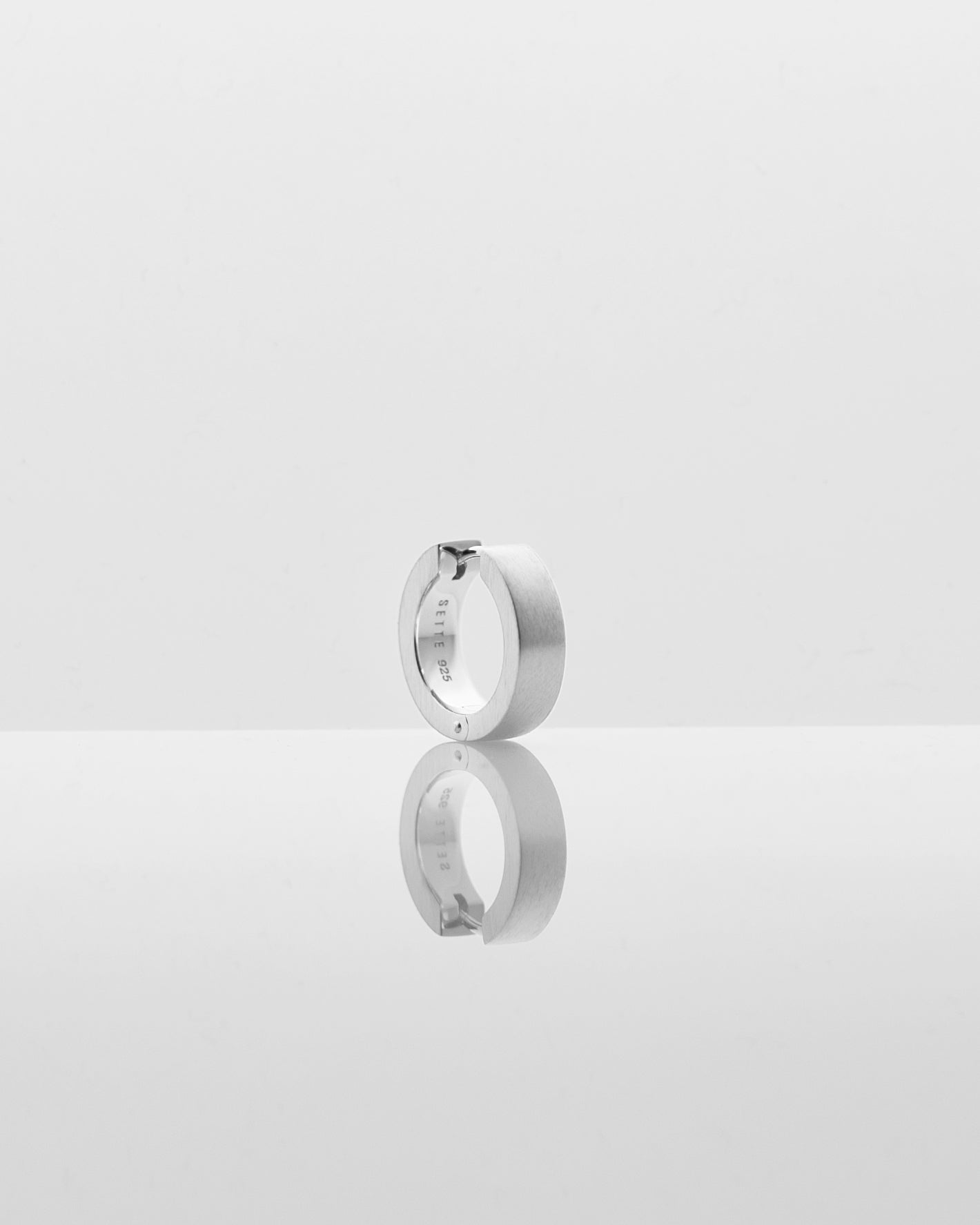 single silver hoop earring on creamy light grey background with reflection