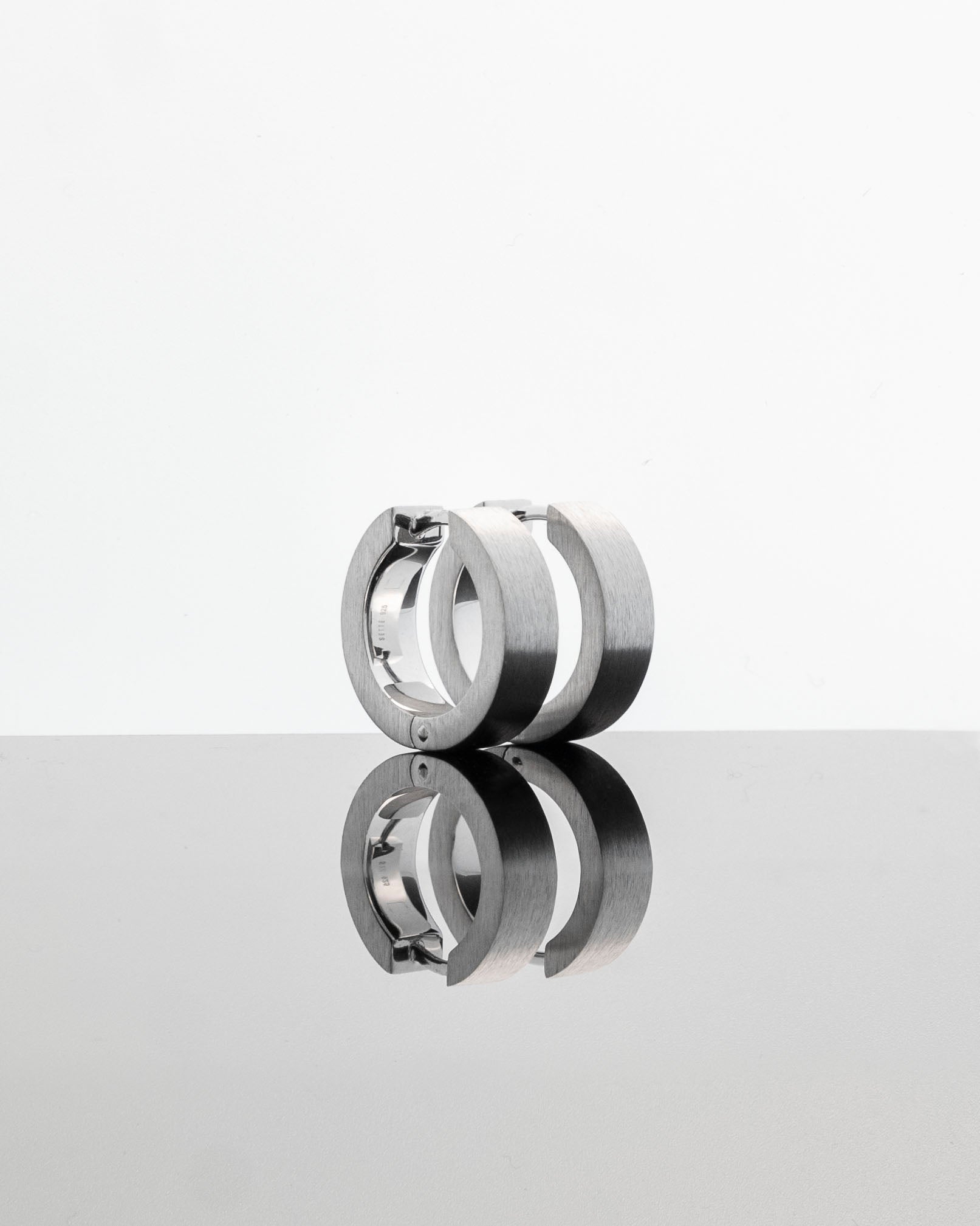 unisex silver hoops reflecting on light gray background brutalist design