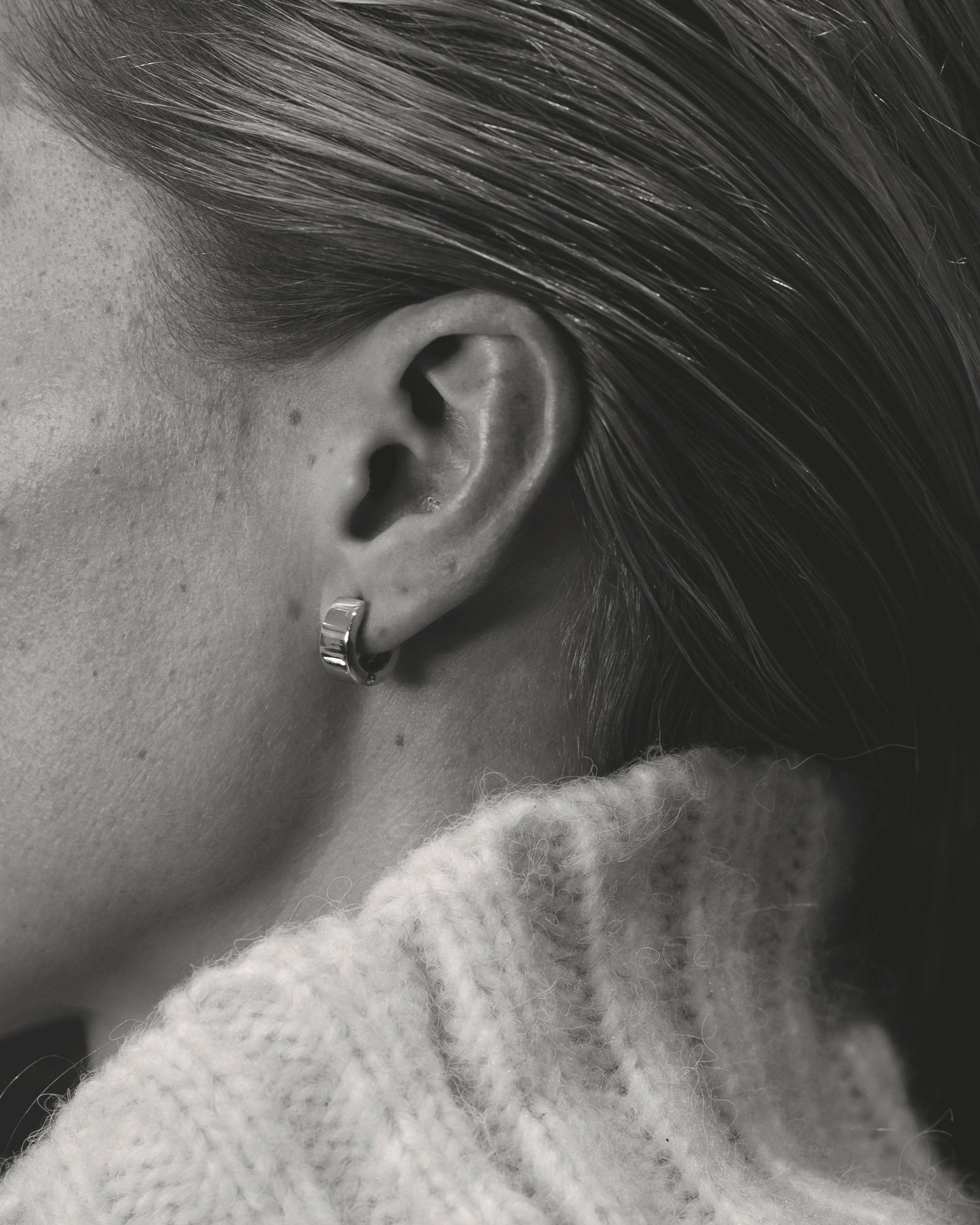 closeup unisex silver hoop earring on model wearing white knit collar