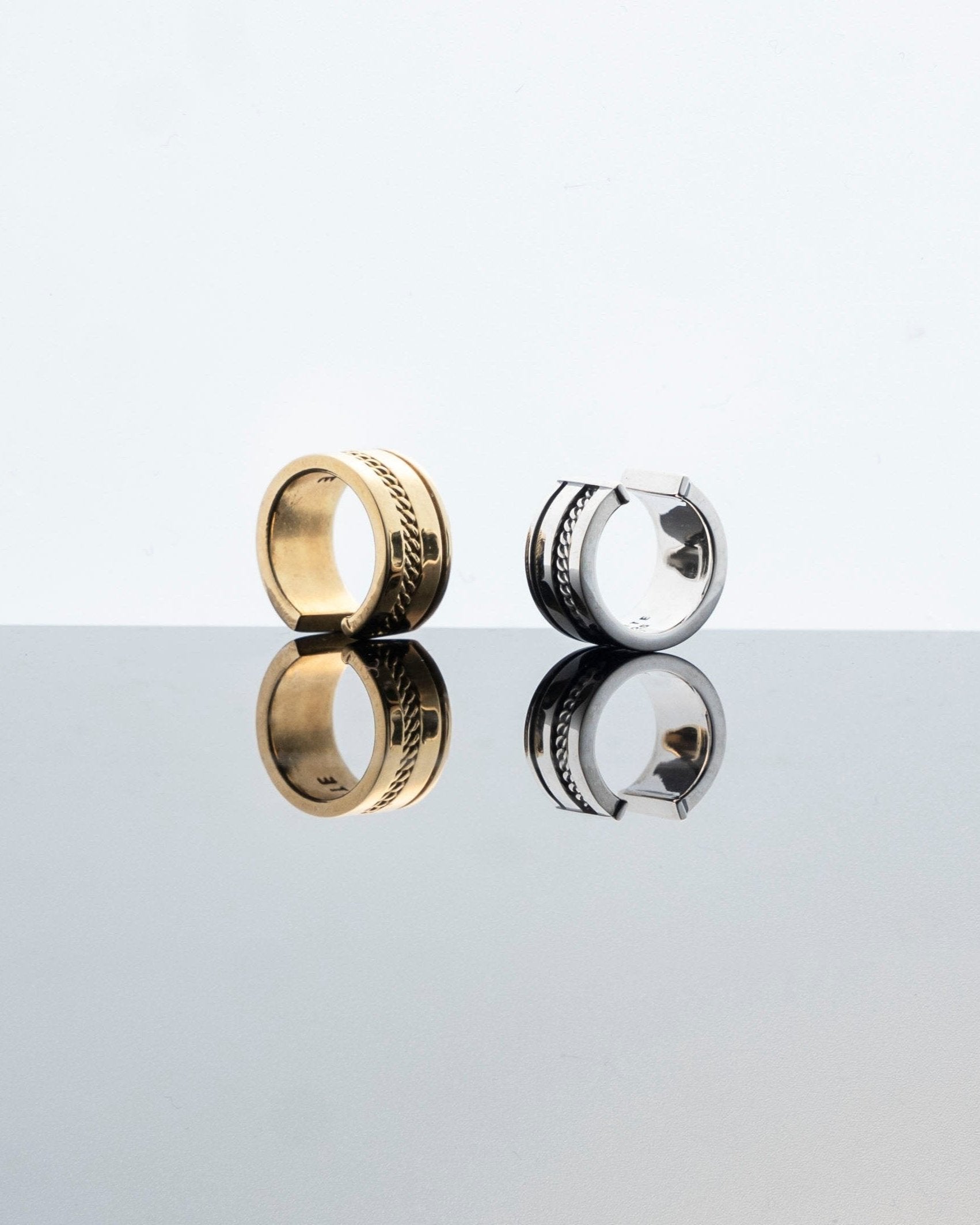 silver and gold ear cuffs with chain detail on grey mirror surface