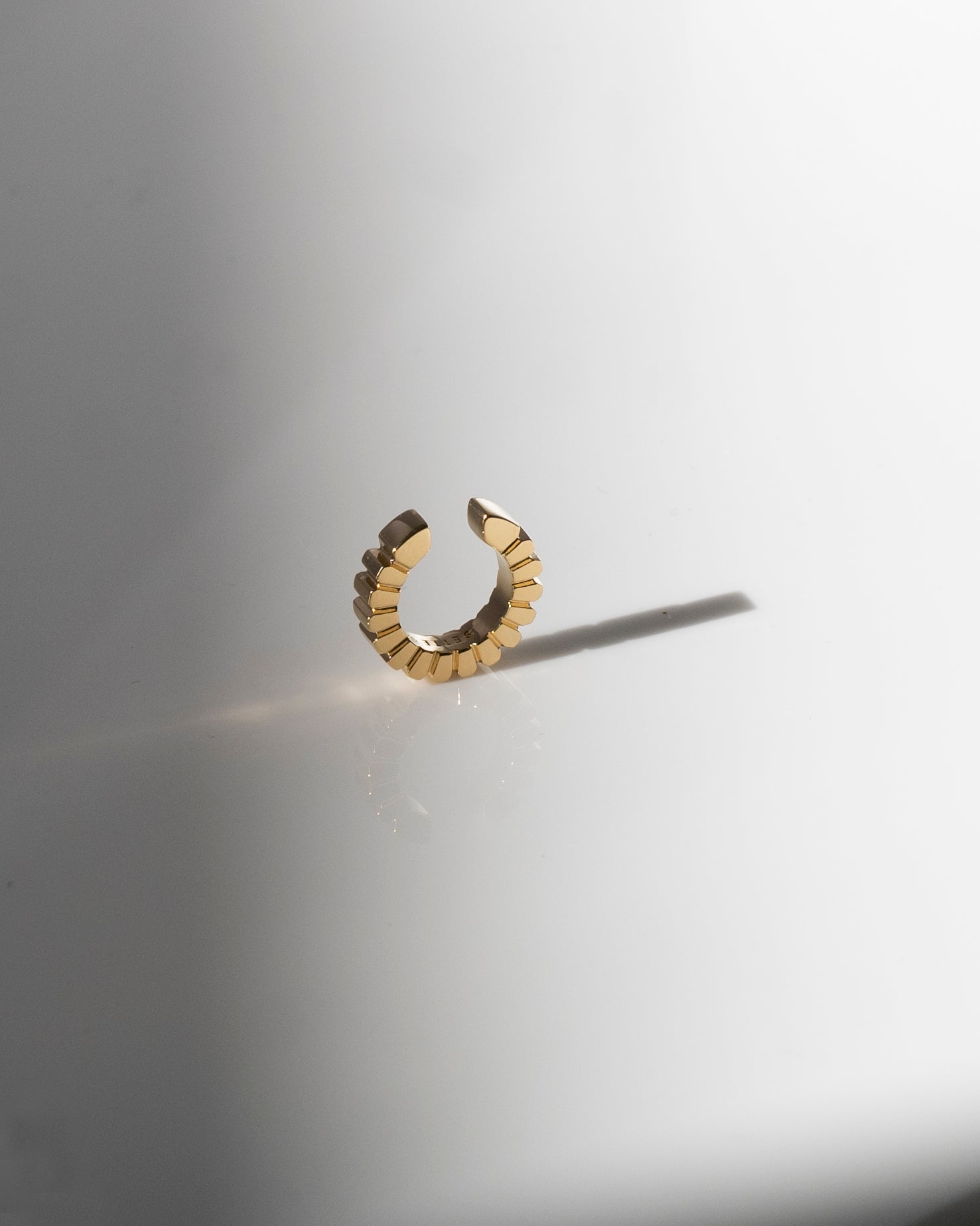 Gold ear cuff on a light grey background with shadow