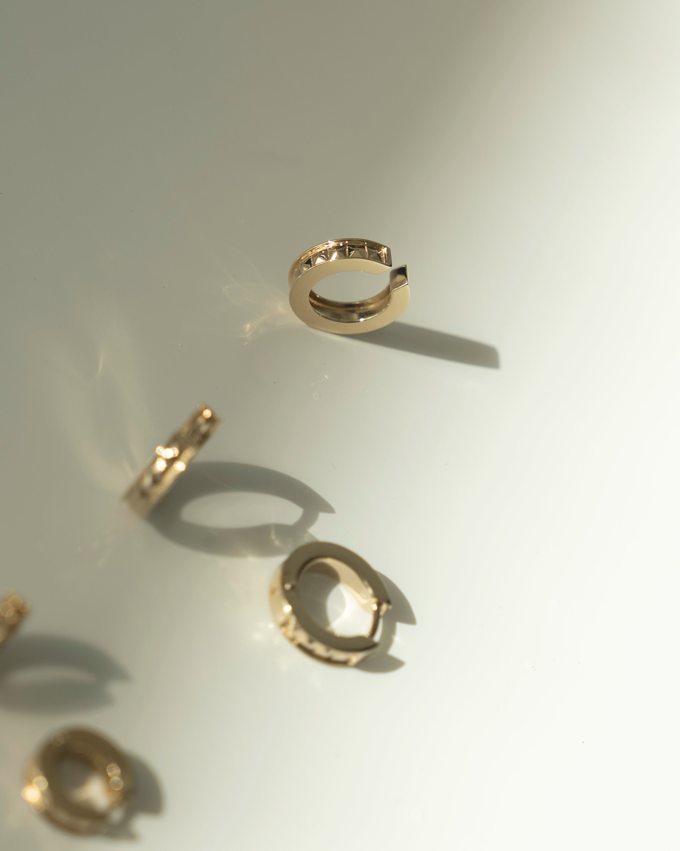 Gold ear cuff with studs with shadow flatlay on light grey background