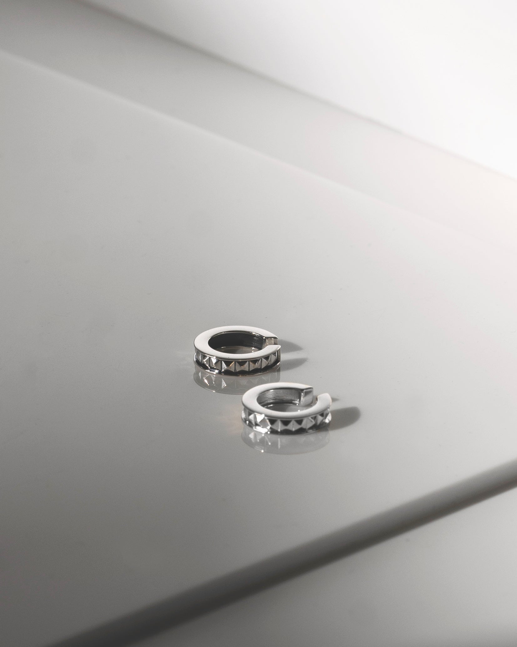 pair of rhodium plated silver ear cuffs on grey reflective background