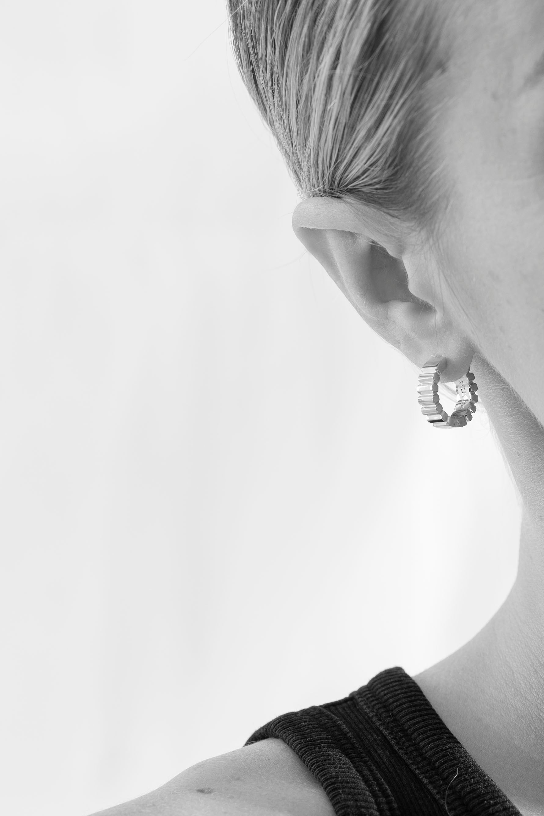 studio sette close-up of a model wearing geometric ridged small hoop earrings with a plain white background