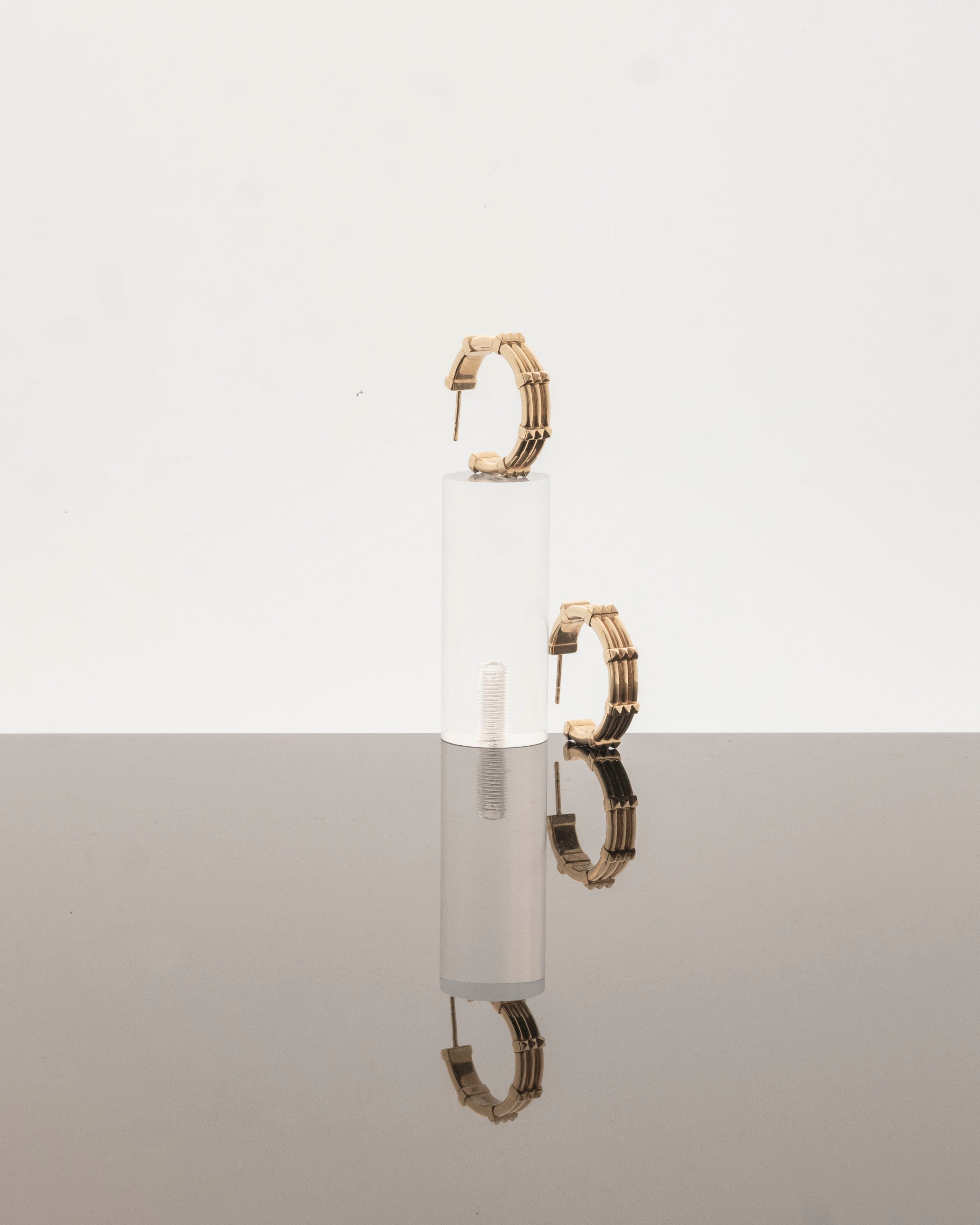 studio sette large hoop earrings displayed on perspex podium on a grey mirrored surface