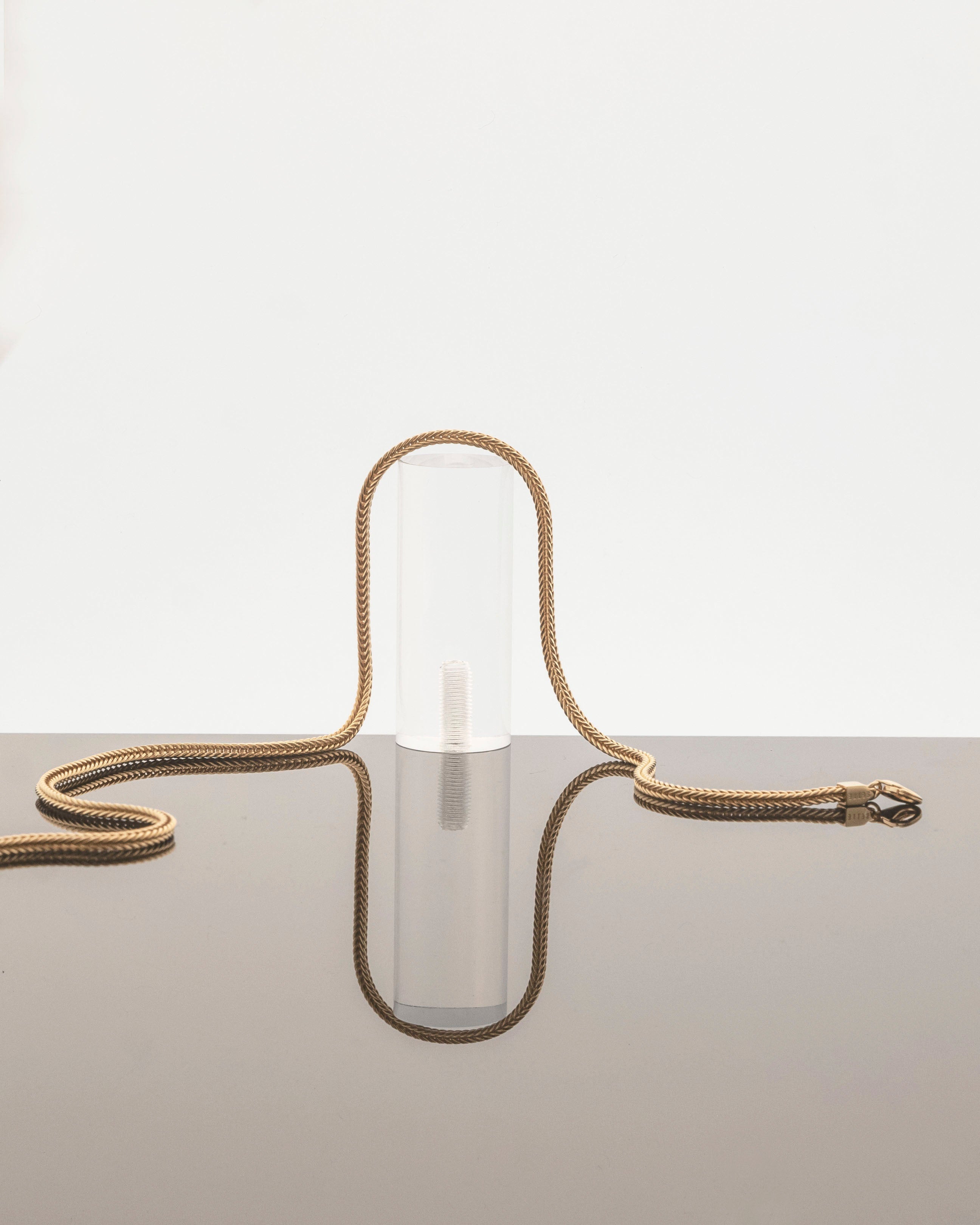 gold plated fox chain laid on perspec podium reflecting on grey mirror