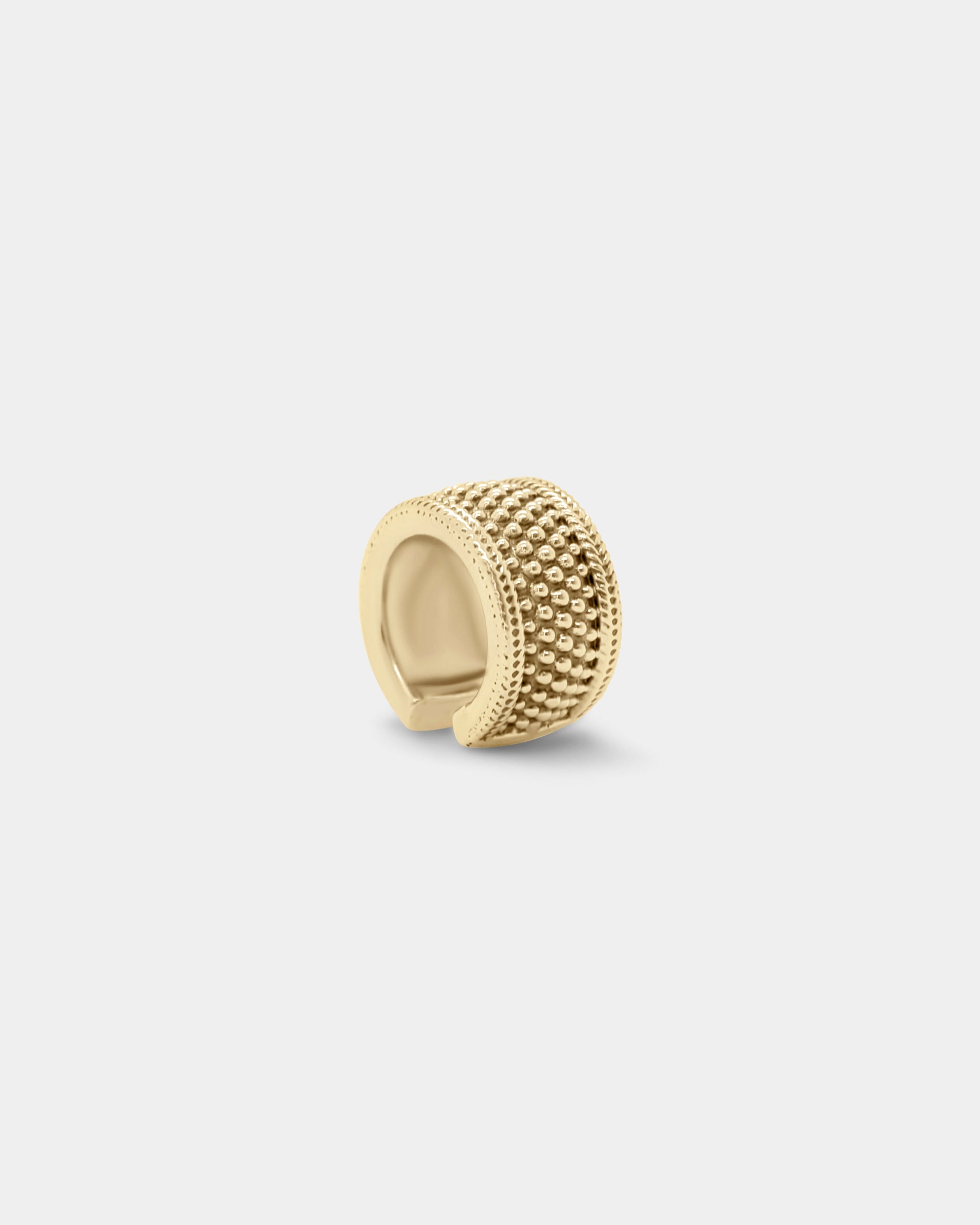 a thick gold ear cuff in a unisex style with stud detailing on a white background by studio sette