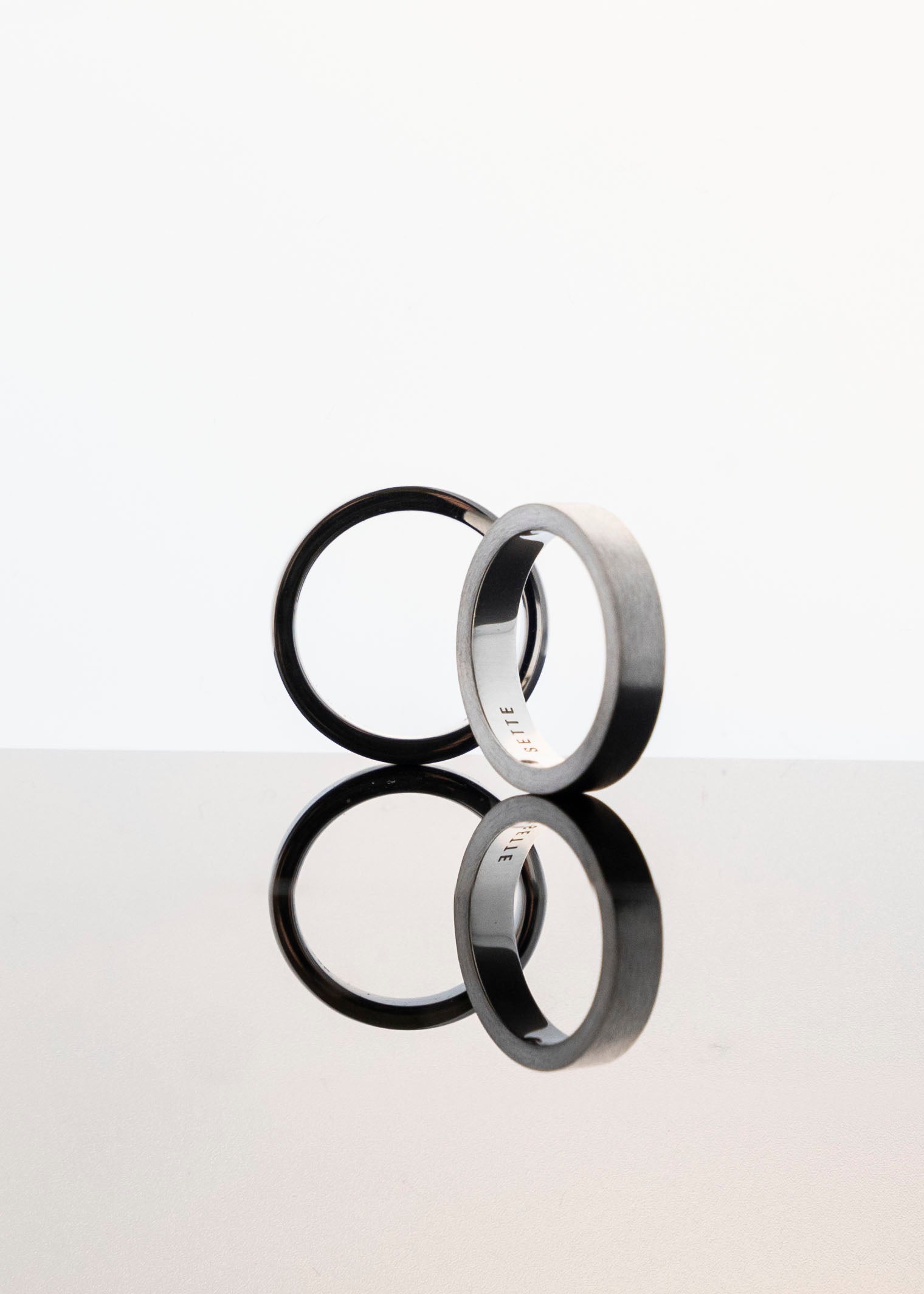 two unisex sillver band rings on light grey background with reflection